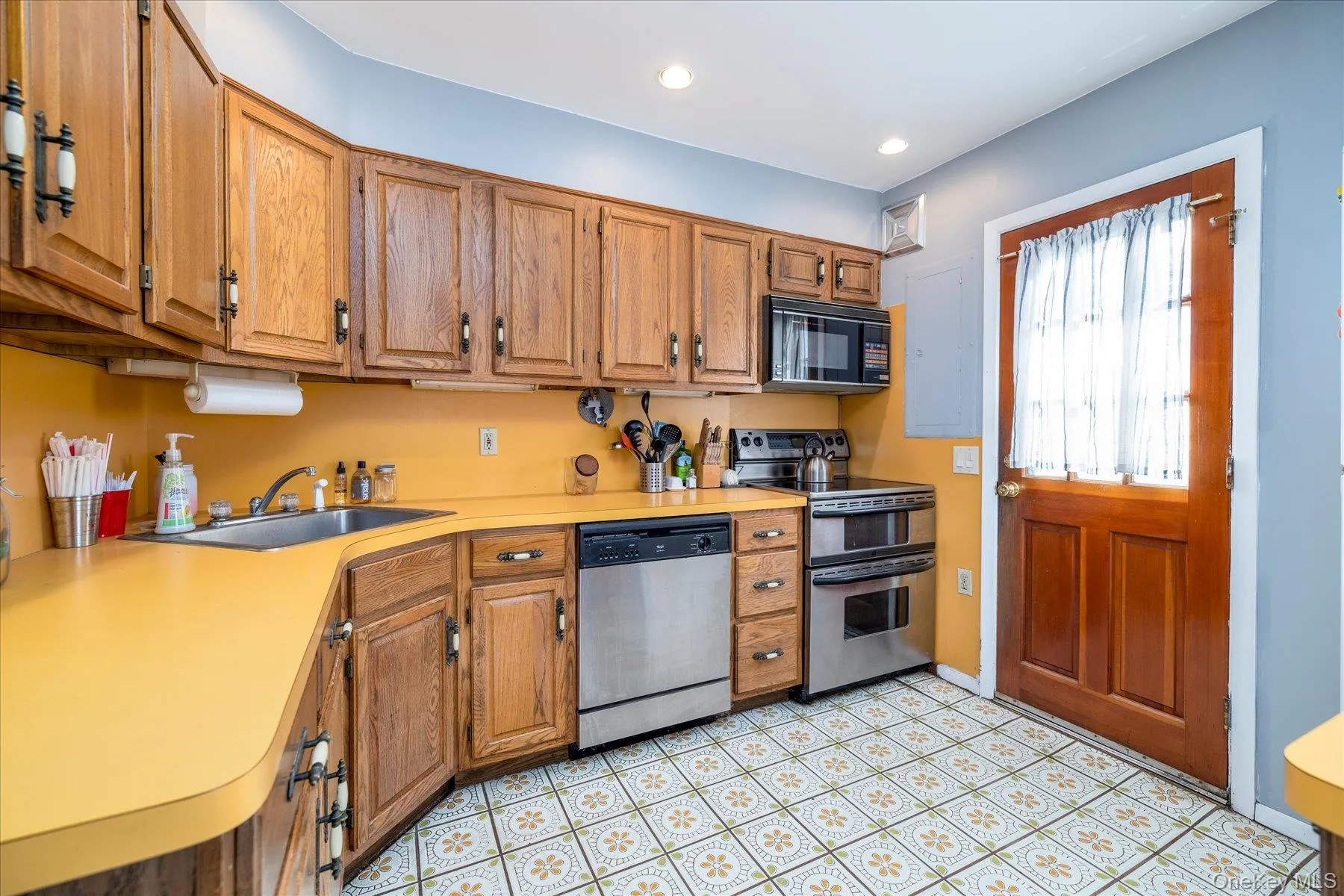 Oak cabinetry with yellow countertops, stainless steel appliances, and patterned floor tiling Oak cabinetry with yellow countertops, stainless steel appliances, and patterned floor tiling