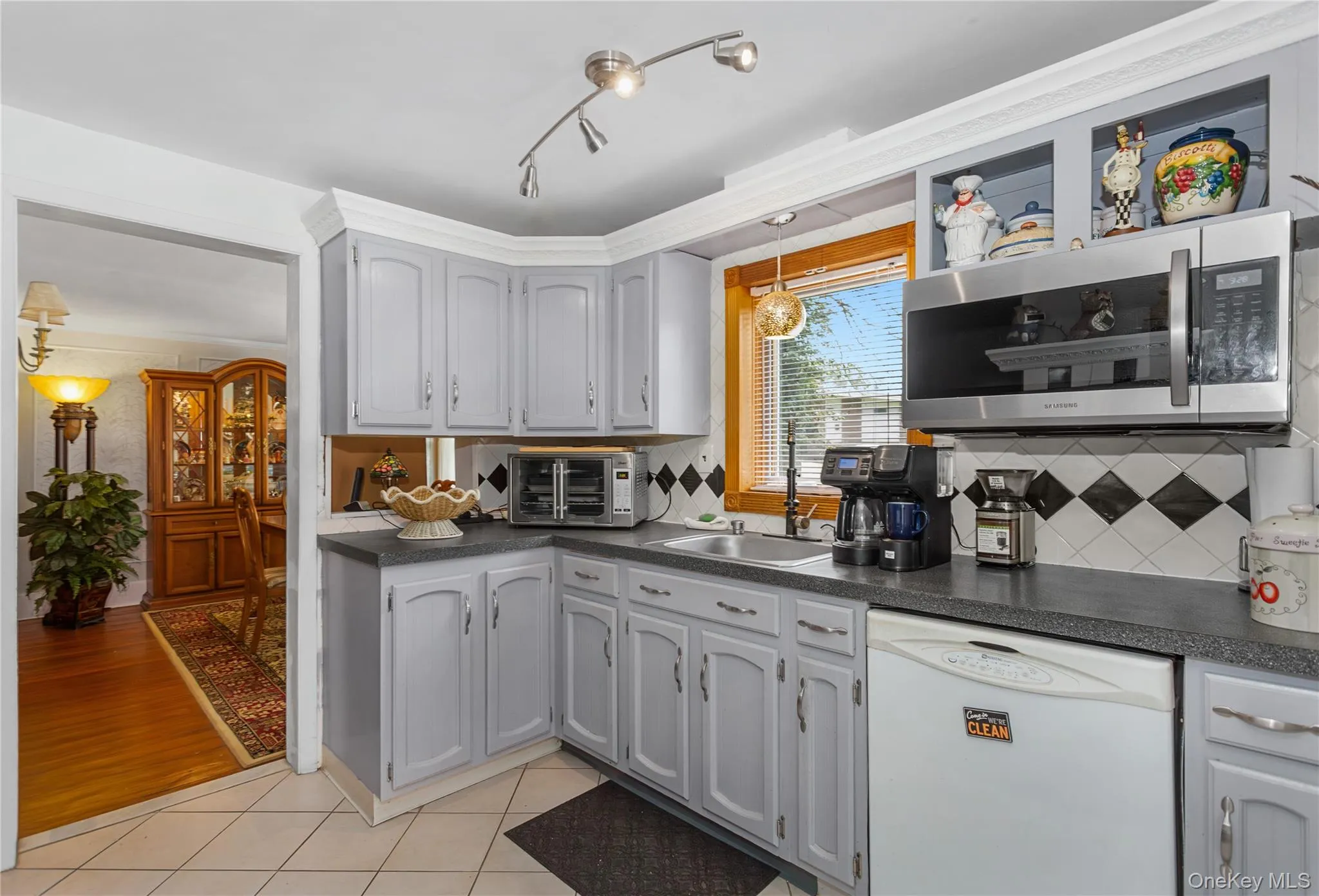 Kitchen with white dishwasher, dark countertops, stainless steel microwave, tasteful backsplash, and crown molding Kitchen with white dishwasher, dark countertops, stainless steel microwave, tasteful backsplash, and crown molding