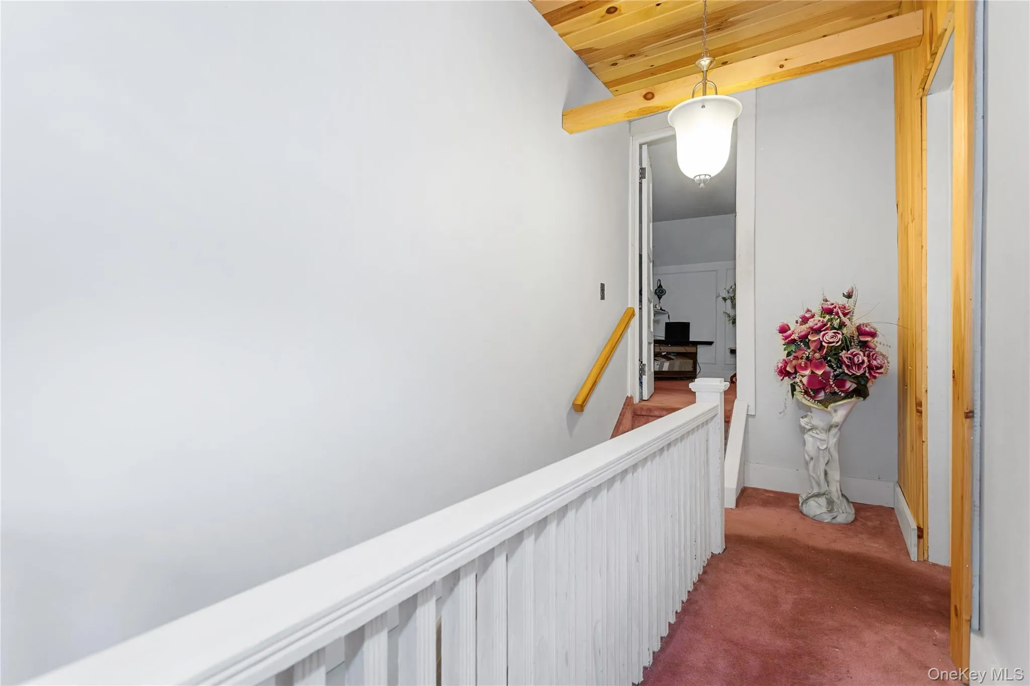 Hallway featuring light carpet, wood ceiling, and an upstairs landing Hallway featuring light carpet, wood ceiling, and an upstairs landing