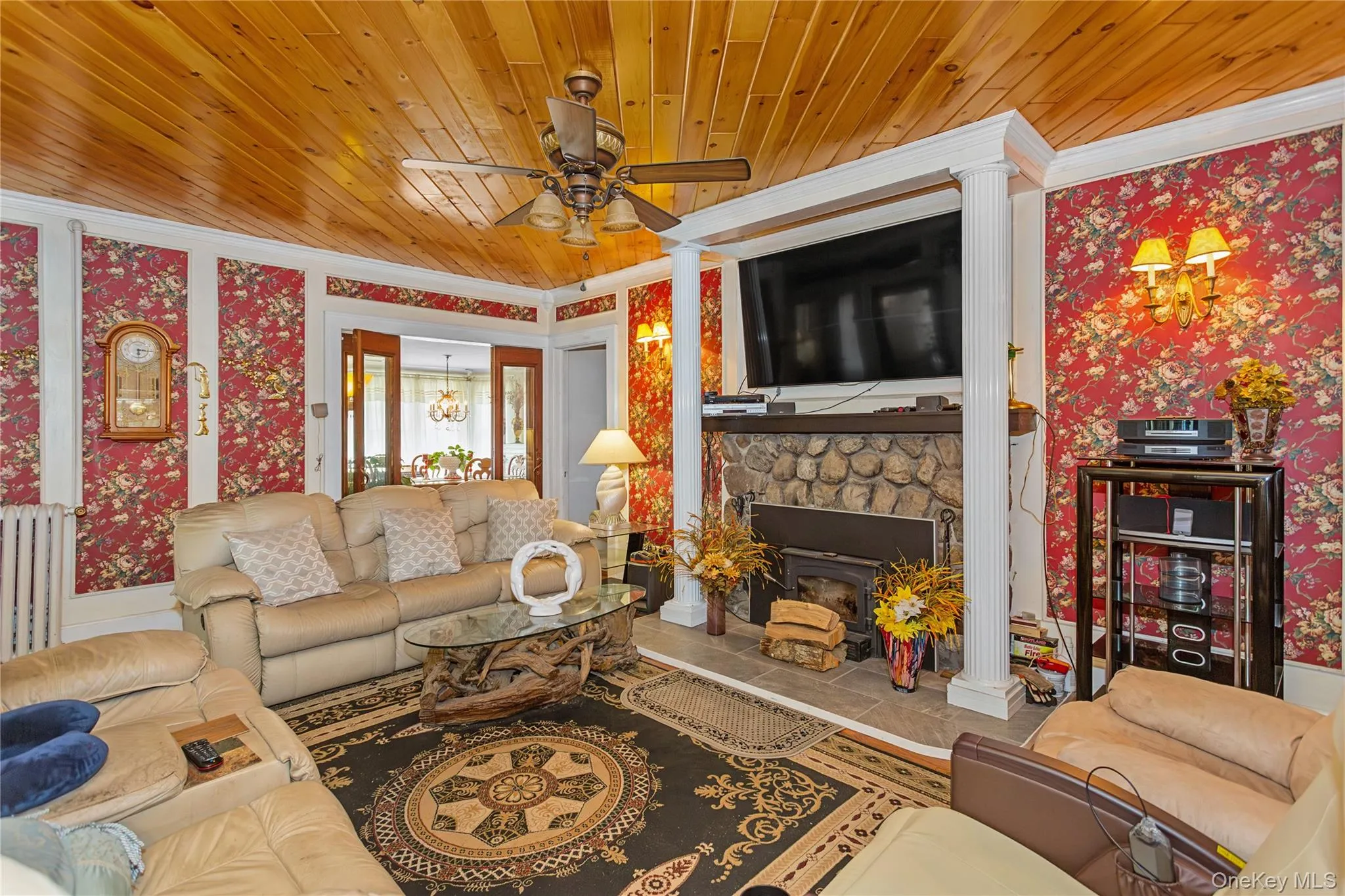 Tiled living room featuring wallpapered walls, wooden ceiling, radiator, a fireplace, and a ceiling fan Tiled living room featuring wallpapered walls, wooden ceiling, radiator, a fireplace, and a ceiling fan