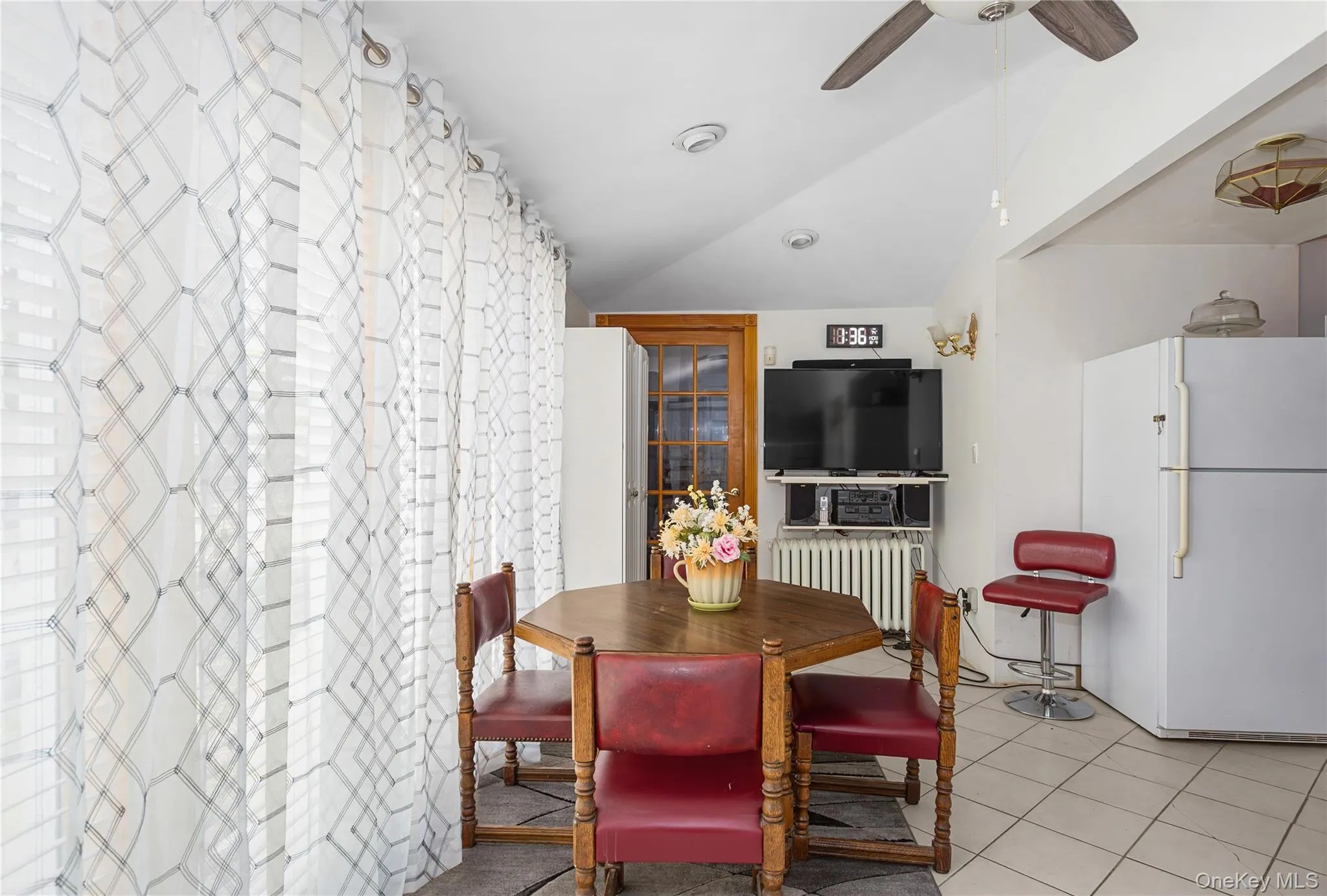 Dining room featuring vaulted ceiling, radiator, light tile patterned flooring, and ceiling fan Dining room featuring vaulted ceiling, radiator, light tile patterned flooring, and ceiling fan