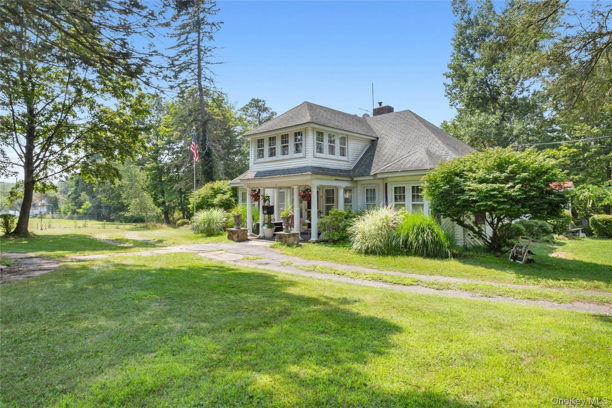 Shingle-style home with a chimney, a front yard, roof with shingles, and covered porch Shingle-style home with a chimney, a front yard, roof with shingles, and covered porch