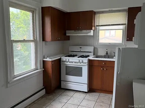 Kitchen featuring white gas range, a baseboard radiator, light countertops, and freestanding refrigerator Kitchen featuring white gas range, a baseboard radiator, light countertops, and freestanding refrigerator