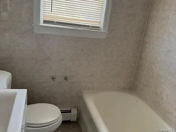 Full bath featuring a bathtub, tile walls, a baseboard radiator, and vanity Full bath featuring a bathtub, tile walls, a baseboard radiator, and vanity