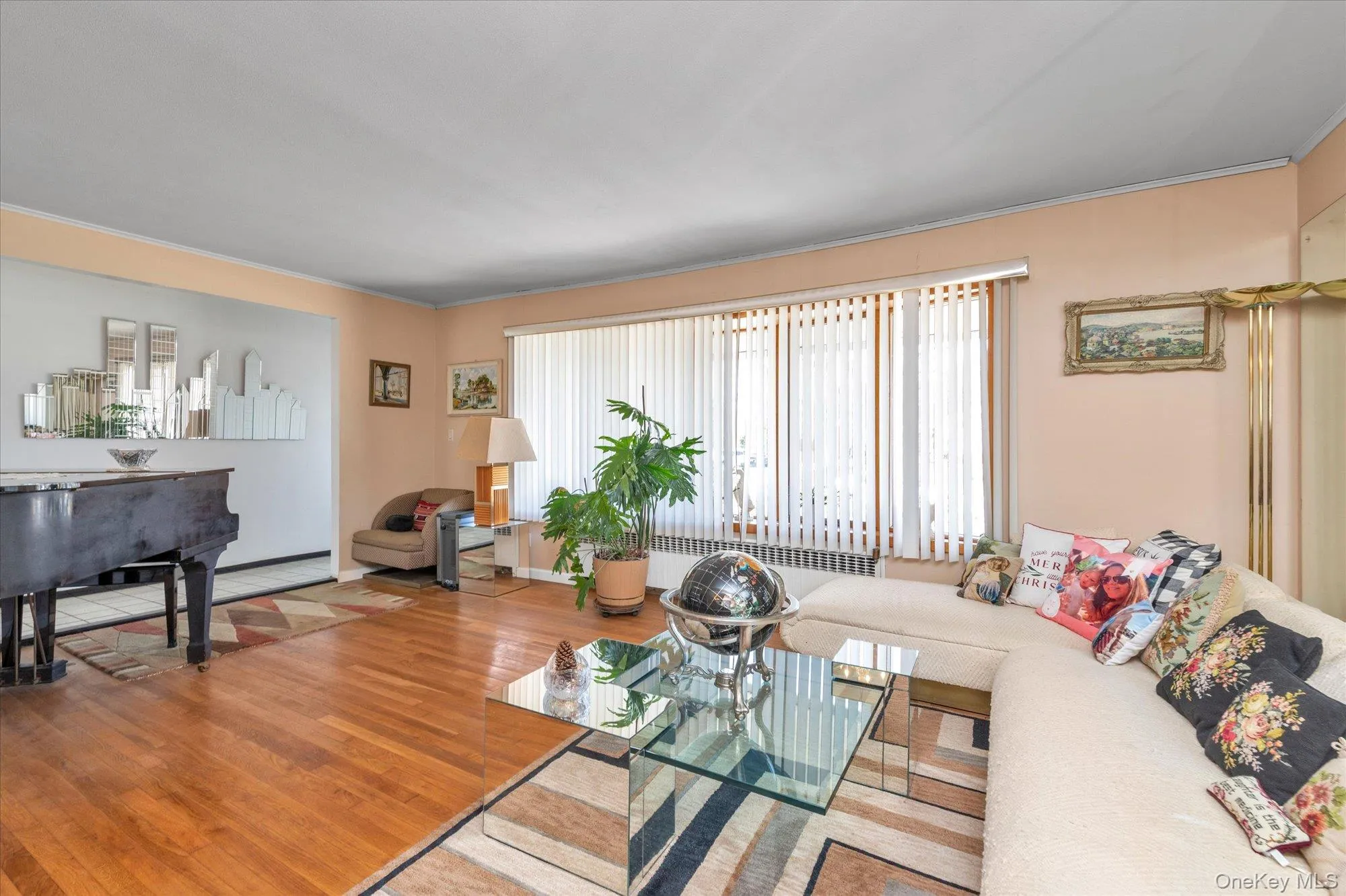 Bright interior space featuring wood-finish flooring, a large picture window with vertical blinds, and a pass-through opening to an additional area Bright interior space featuring wood-finish flooring, a large picture window with vertical blinds, and a pass-through opening to an additional area
