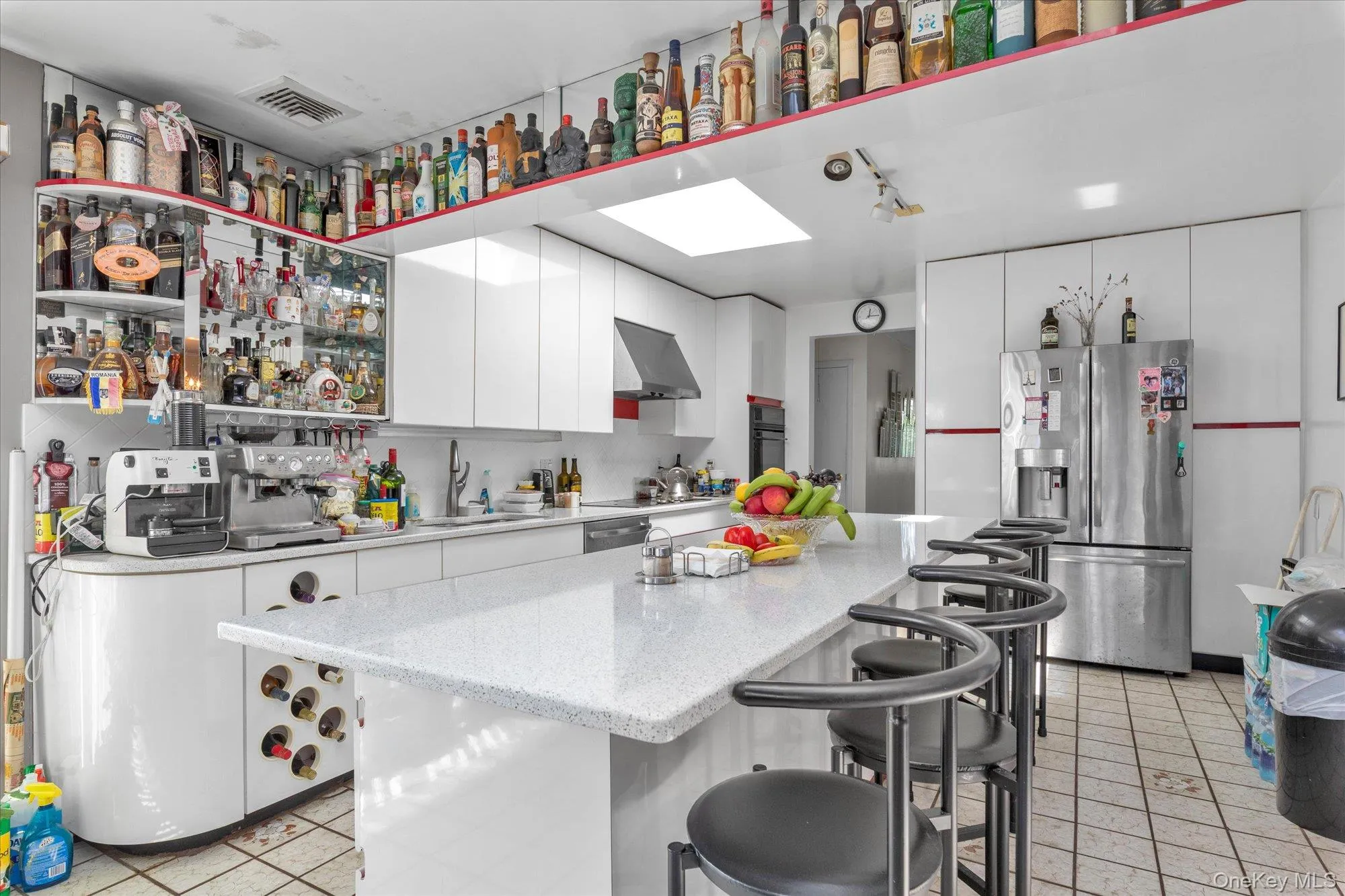 Open-concept kitchen featuring an expansive island with seating, white cabinetry, a built-in wine rack, and a skylight Open-concept kitchen featuring an expansive island with seating, white cabinetry, a built-in wine rack, and a skylight