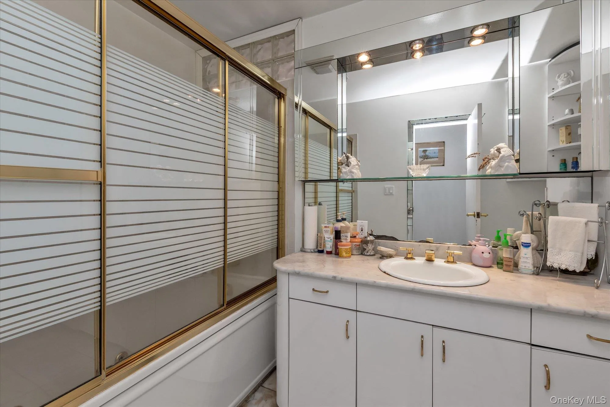 Bathroom vanity with an integrated sink, polished brass fixtures, and an expansive mirror featuring recessed lighting Bathroom vanity with an integrated sink, polished brass fixtures, and an expansive mirror featuring recessed lighting
