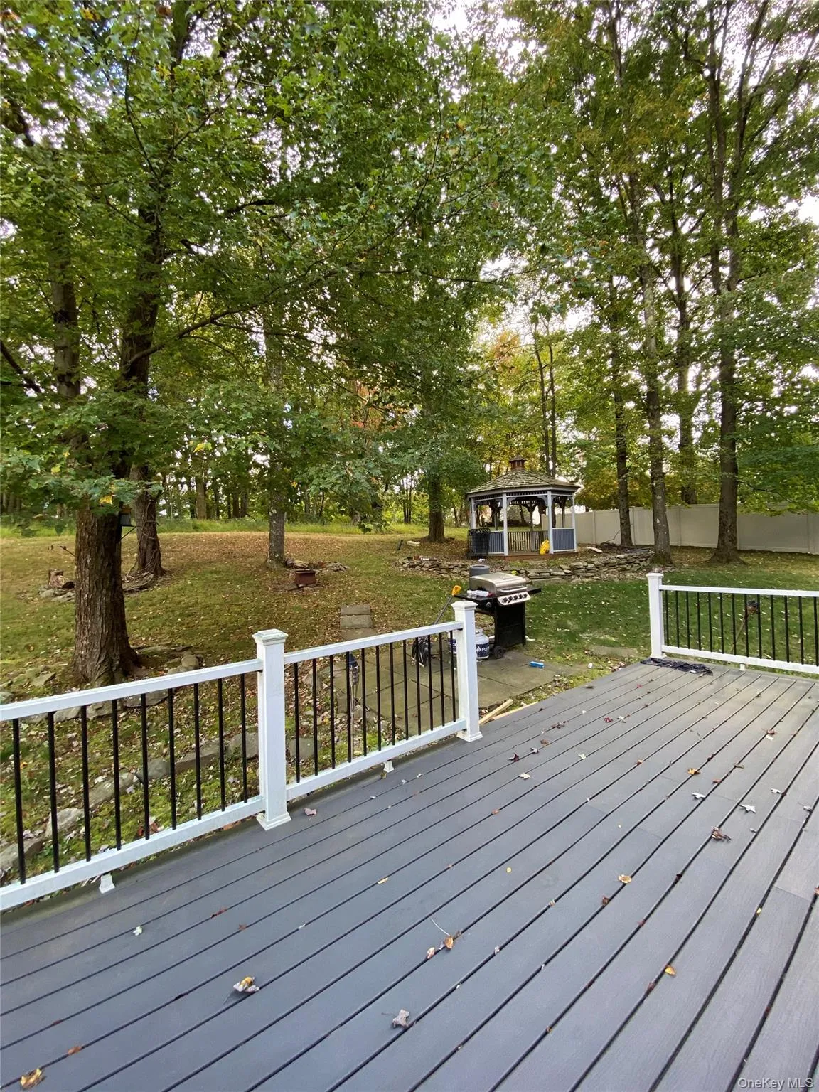 The property features a spacious outdoor deck with white railings, overlooking a large yard with mature trees and a gazebo The property features a spacious outdoor deck with white railings, overlooking a large yard with mature trees and a gazebo