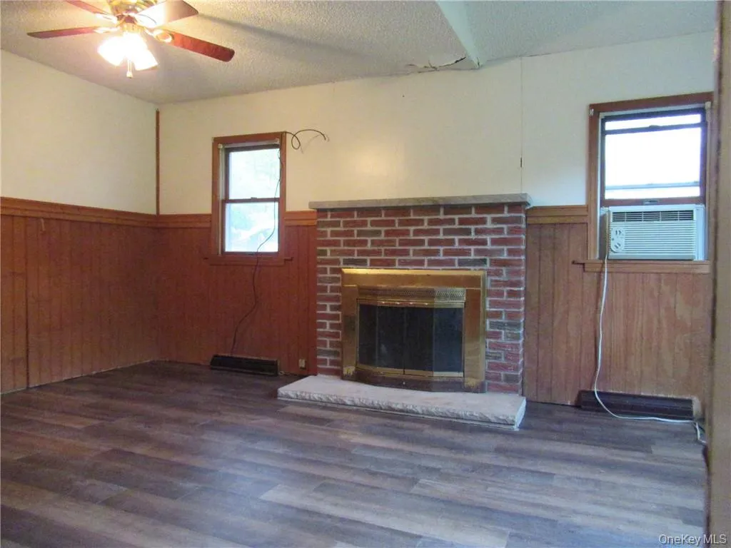 Unfurnished living room featuring a textured ceiling, dark wood-type flooring, ceiling fan, a fireplace, and cooling unit Unfurnished living room featuring a textured ceiling, dark wood-type flooring, ceiling fan, a fireplace, and cooling unit