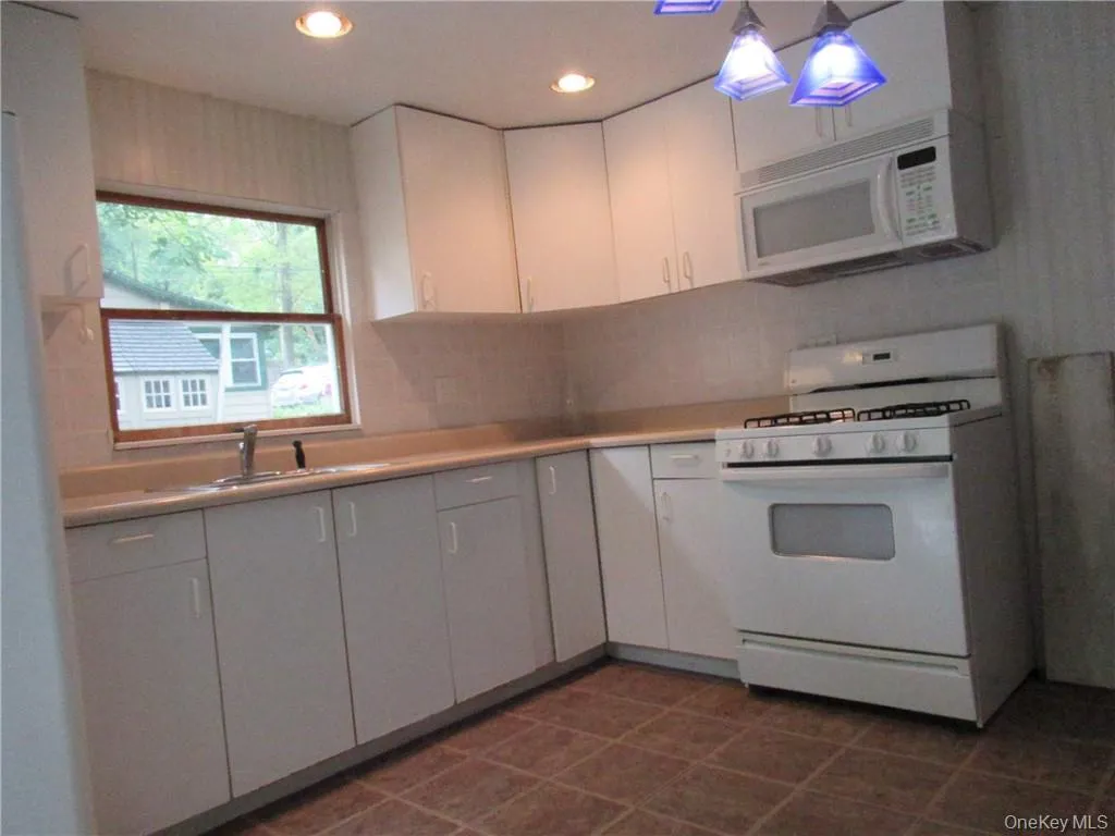 Kitchen featuring dark tile patterned floors, white appliances, white cabinets, backsplash, and sink Kitchen featuring dark tile patterned floors, white appliances, white cabinets, backsplash, and sink
