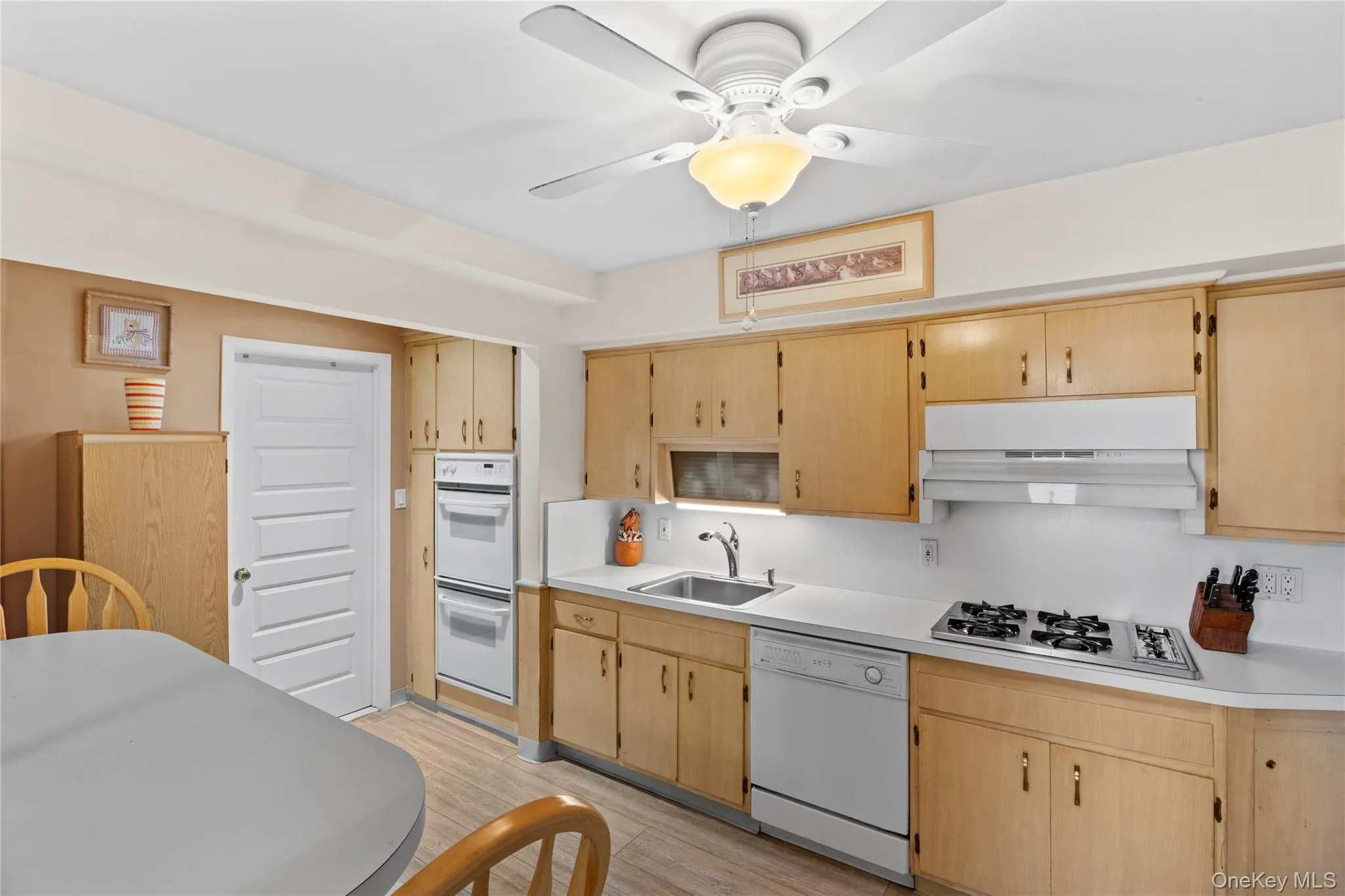 The kitchen features light wood cabinetry, white countertops, and a ceiling fan with integrated lighting The kitchen features light wood cabinetry, white countertops, and a ceiling fan with integrated lighting