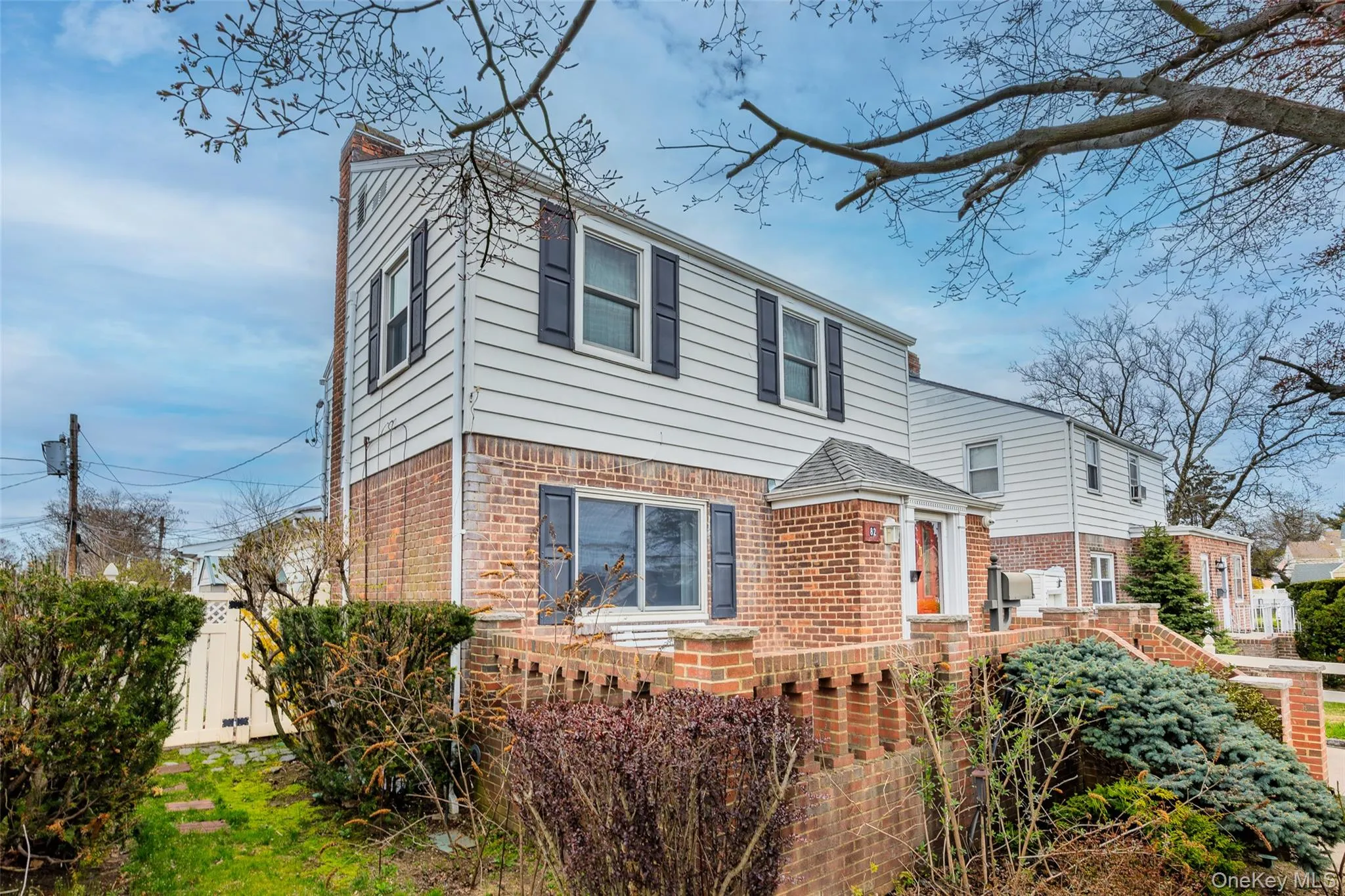 The property features a brick and siding exterior with dark shutters, a front porch with a covered entry, and a fenced yard with established plantings The property features a brick and siding exterior with dark shutters, a front porch with a covered entry, and a fenced yard with established plantings