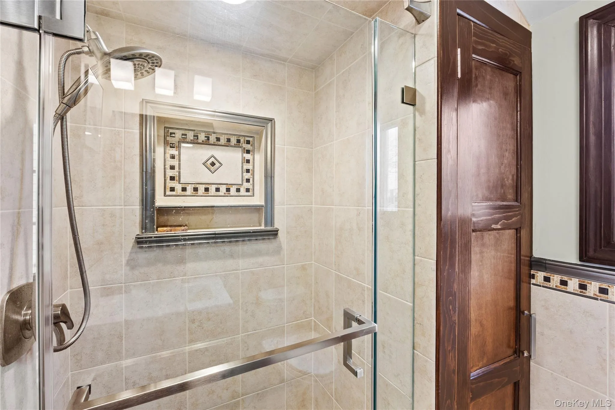 The shower features a handheld showerhead, a tiled niche with decorative accents. The shower features a handheld showerhead, a tiled niche with decorative accents.