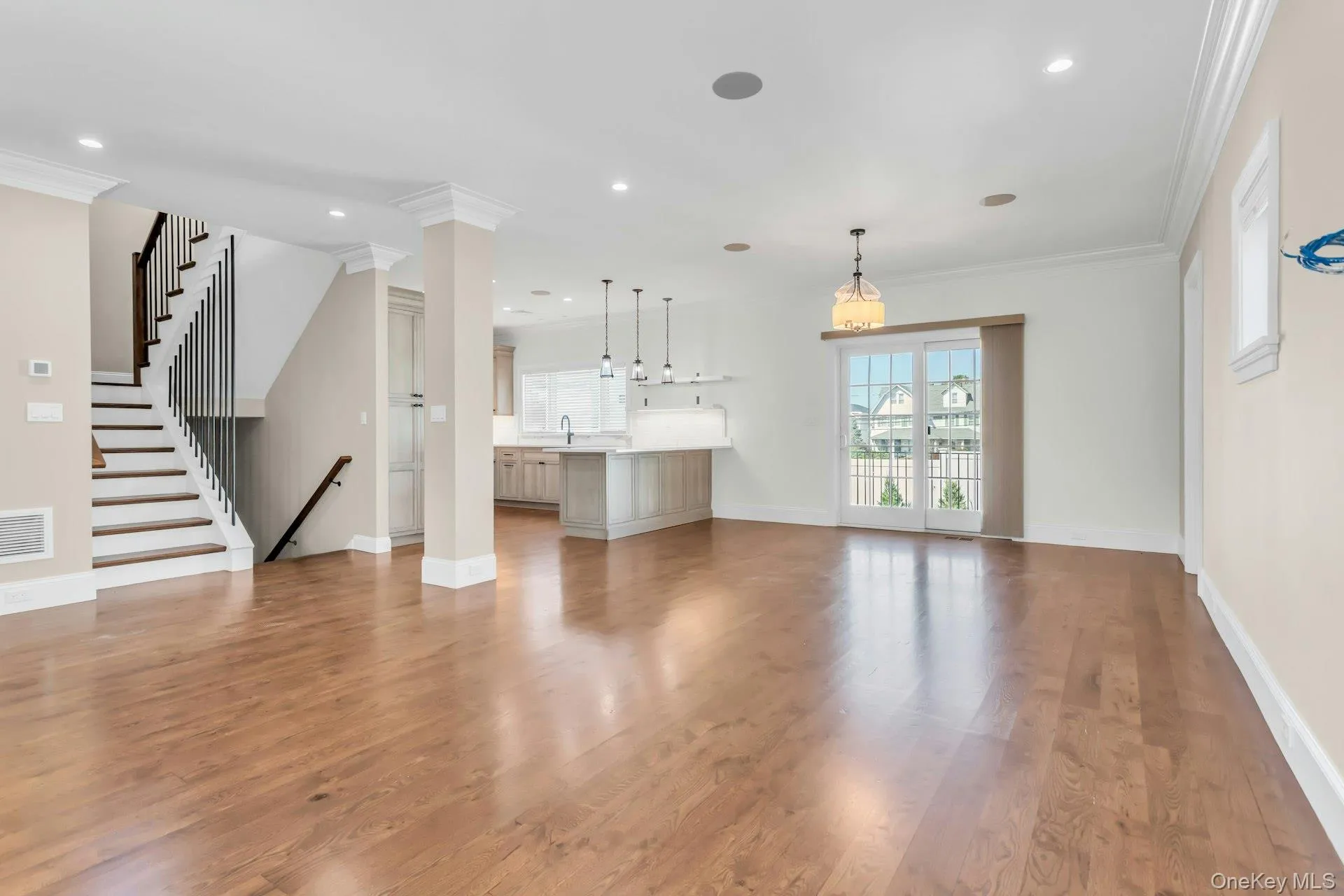 Open-concept living space featuring hardwood floors, a staircase with dark wood handrails, and a kitchen with an island and pendant lights Open-concept living space featuring hardwood floors, a staircase with dark wood handrails, and a kitchen with an island and pendant lights