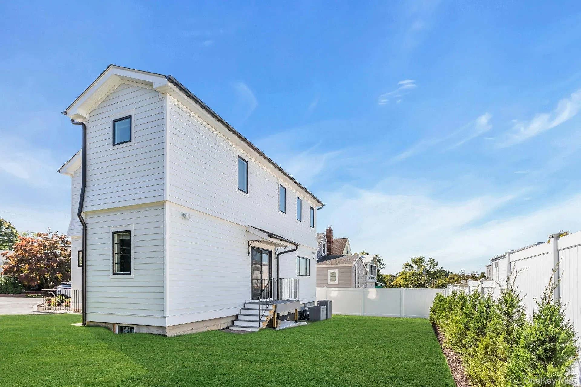 The property features white siding, dark-trimmed windows, a well-maintained lawn, and a white privacy fence The property features white siding, dark-trimmed windows, a well-maintained lawn, and a white privacy fence