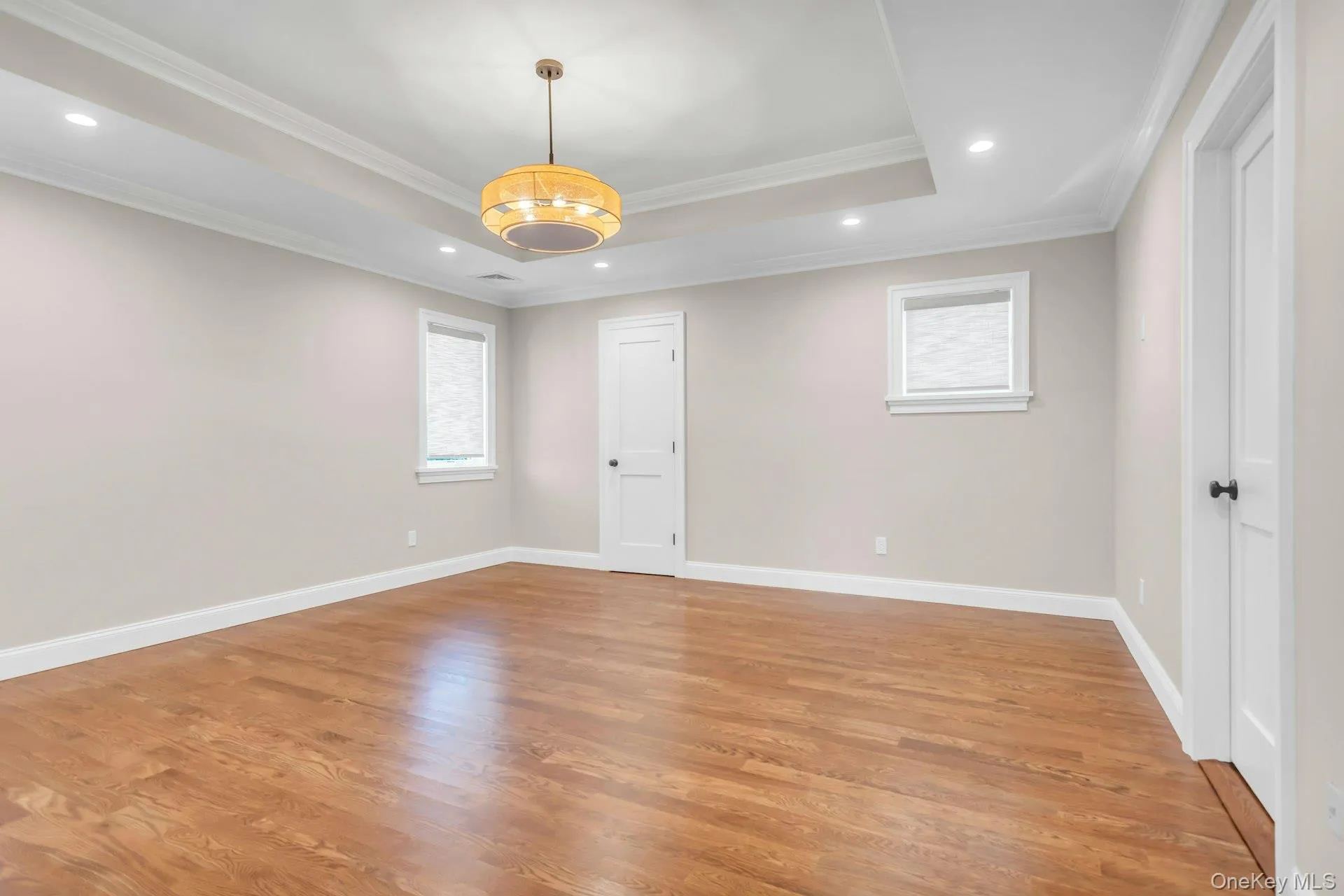 Spacious room featuring hardwood flooring, a tray ceiling with recessed lighting, and a decorative pendant light fixture Spacious room featuring hardwood flooring, a tray ceiling with recessed lighting, and a decorative pendant light fixture