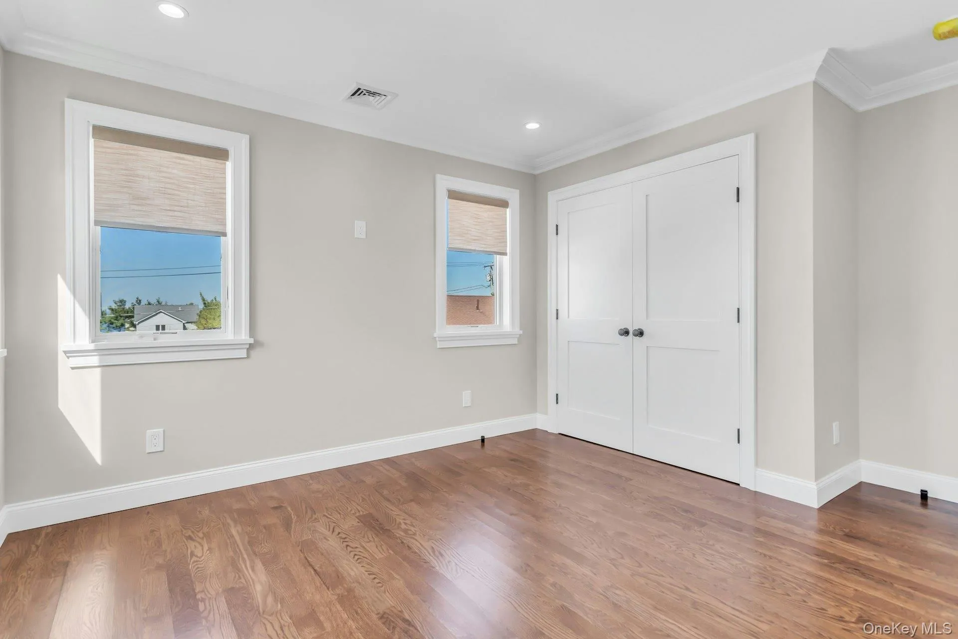 This room features hardwood floors, light gray walls, white trim, and two windows with shades This room features hardwood floors, light gray walls, white trim, and two windows with shades