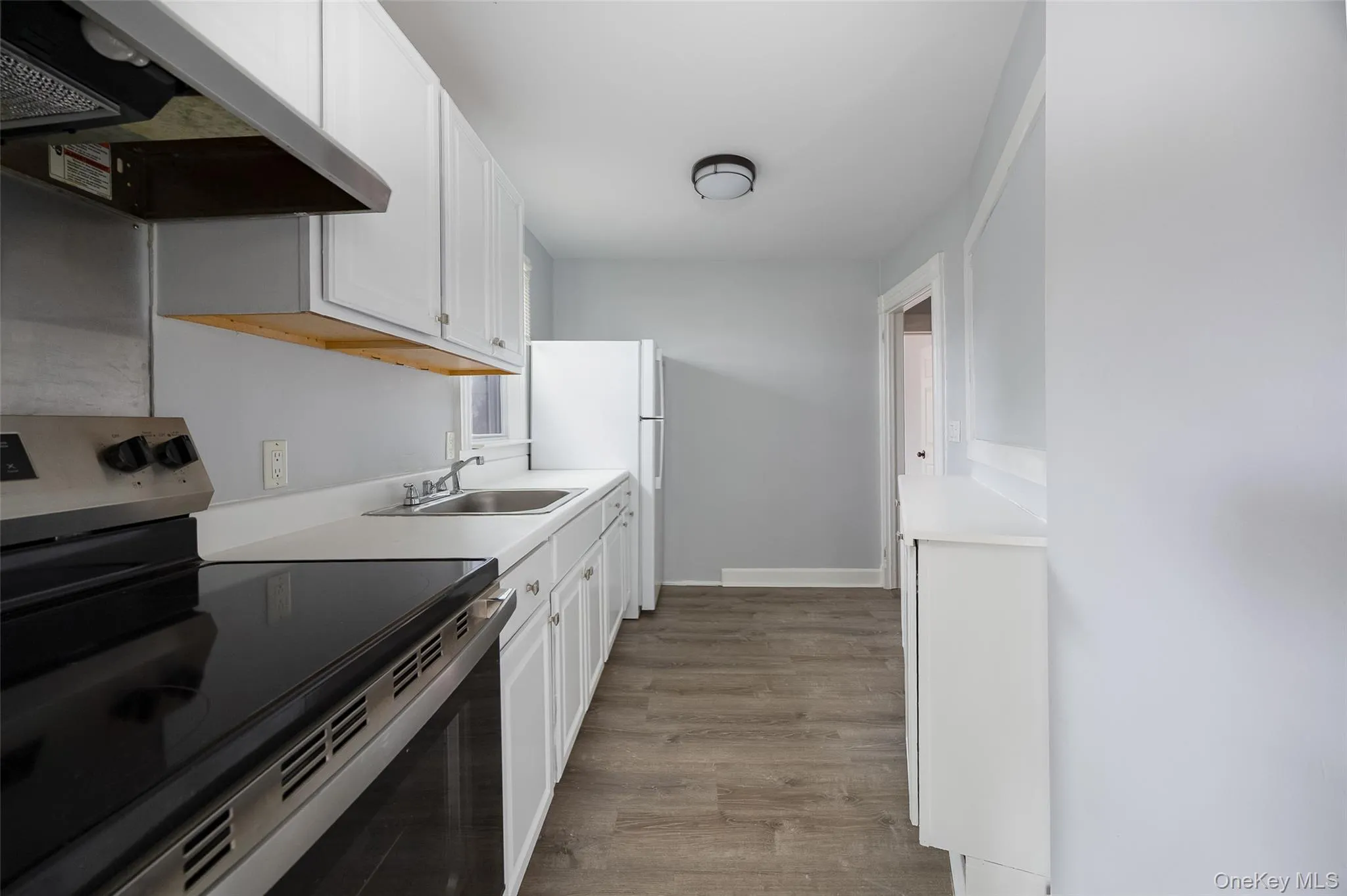 Galley kitchen featuring wood-finish flooring, white cabinetry, solid surface countertops, a stainless steel range, and a white refrigerator Galley kitchen featuring wood-finish flooring, white cabinetry, solid surface countertops, a stainless steel range, and a white refrigerator