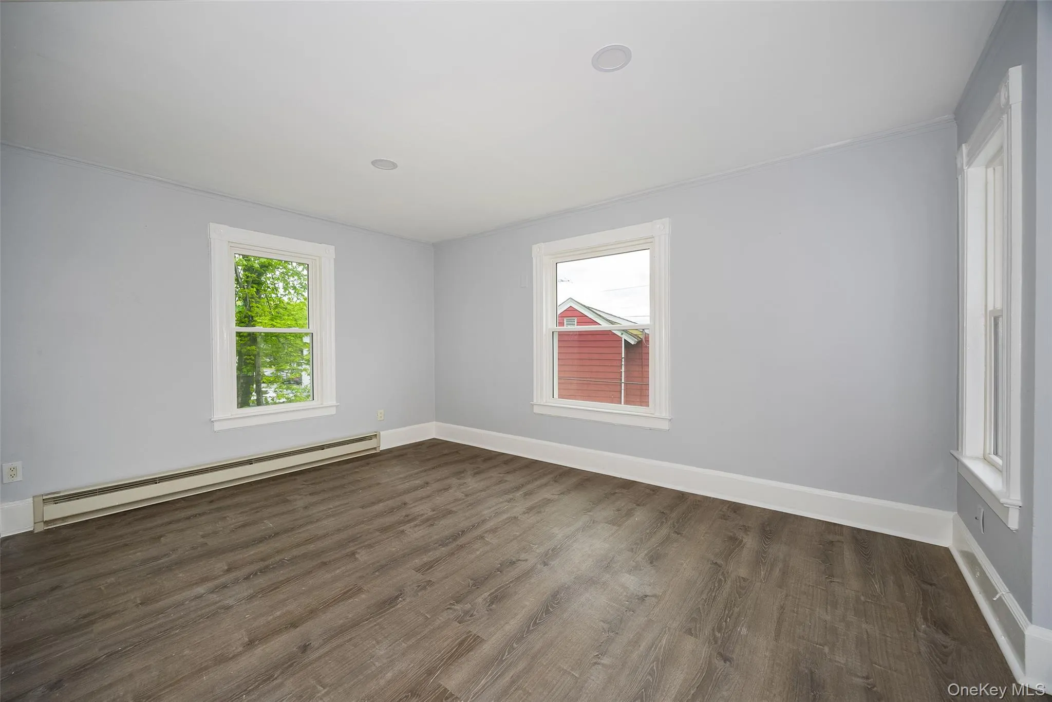 Gray toned room featuring two windows with white trim, wood-finish flooring, recessed ceiling lighting, and baseboard heating Gray toned room featuring two windows with white trim, wood-finish flooring, recessed ceiling lighting, and baseboard heating