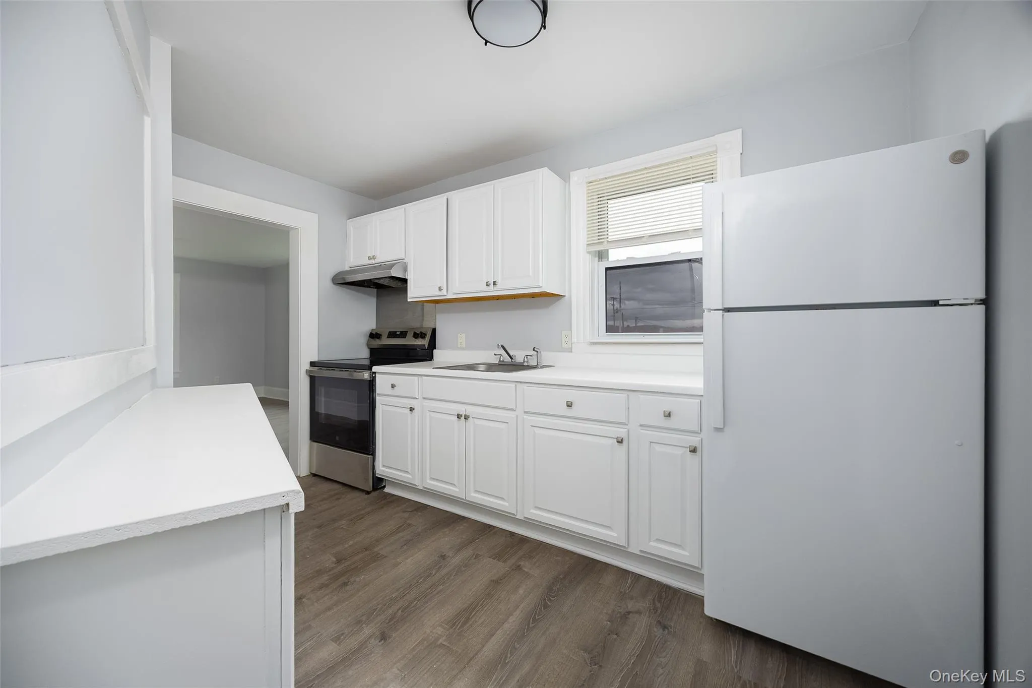Kitchen featuring white cabinetry, white countertops, stainless steel range and range hood, and wood-finish flooring Kitchen featuring white cabinetry, white countertops, stainless steel range and range hood, and wood-finish flooring