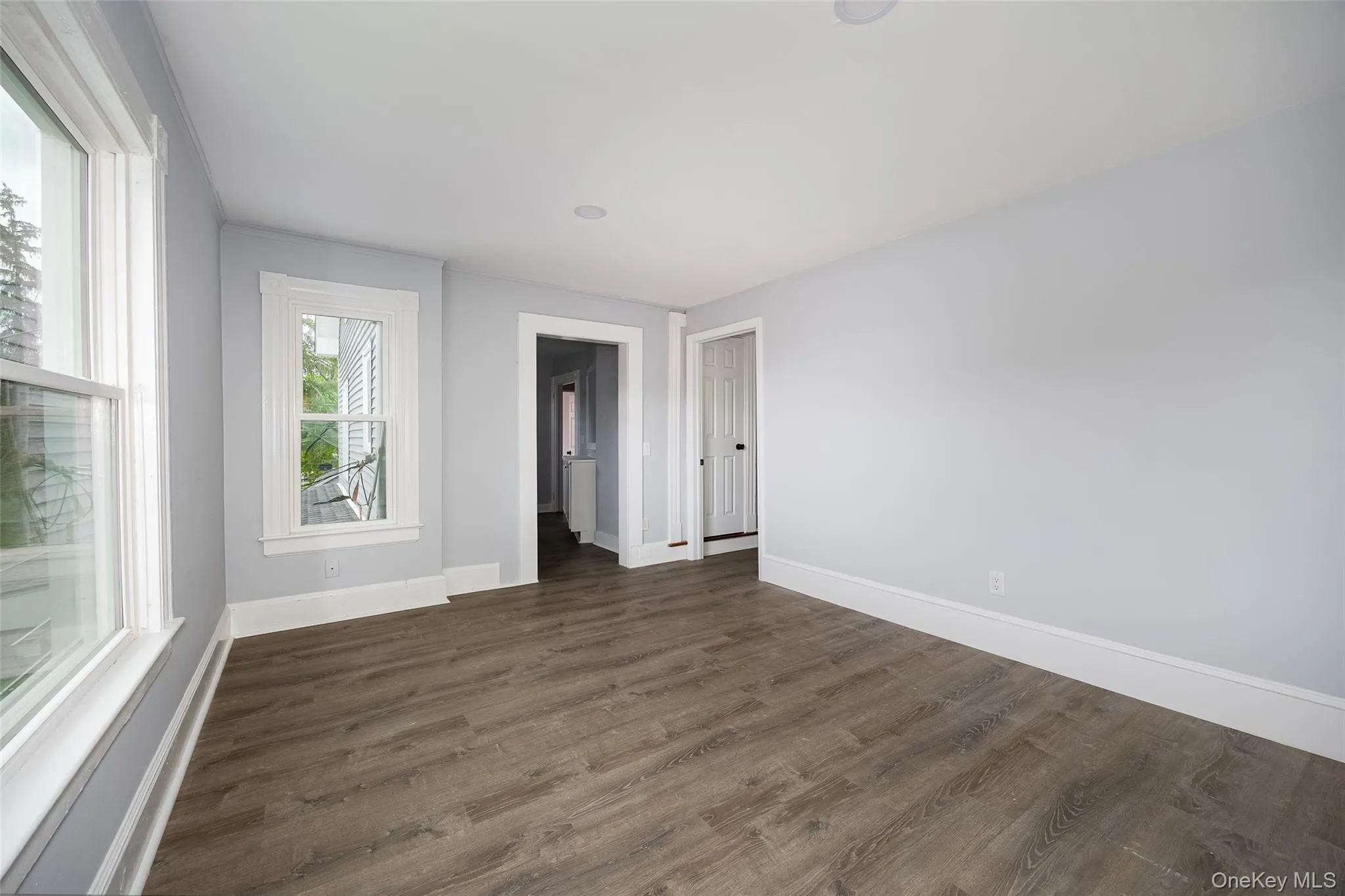 Spacious room featuring wood-finish flooring, light grey wall paint, and white trim Spacious room featuring wood-finish flooring, light grey wall paint, and white trim