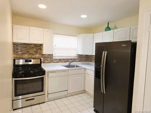 The kitchen features white cabinetry, a tiled backsplash, and stainless steel appliances including a range and a side-by-side refrigerator The kitchen features white cabinetry, a tiled backsplash, and stainless steel appliances including a range and a side-by-side refrigerator