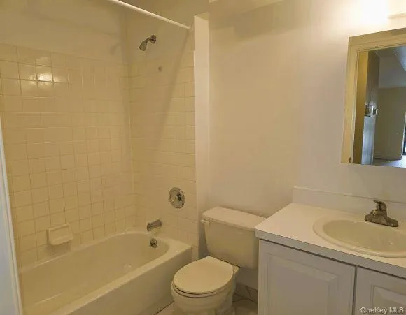 Main bathroom featuring a white bathtub with tiled walls, a toilet, a vanity with a white countertop, and a mirror Main bathroom featuring a white bathtub with tiled walls, a toilet, a vanity with a white countertop, and a mirror