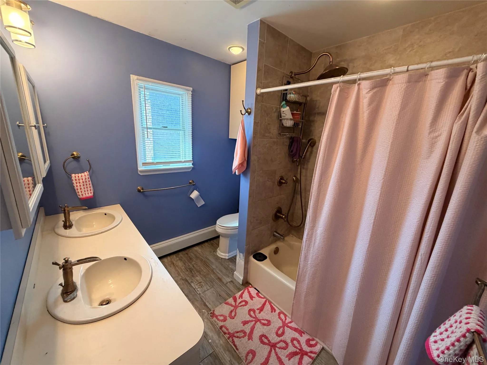 Bathroom featuring a double vanity with white countertops, a window with blinds, and a combination shower and bathtub with tile surround Bathroom featuring a double vanity with white countertops, a window with blinds, and a combination shower and bathtub with tile surround