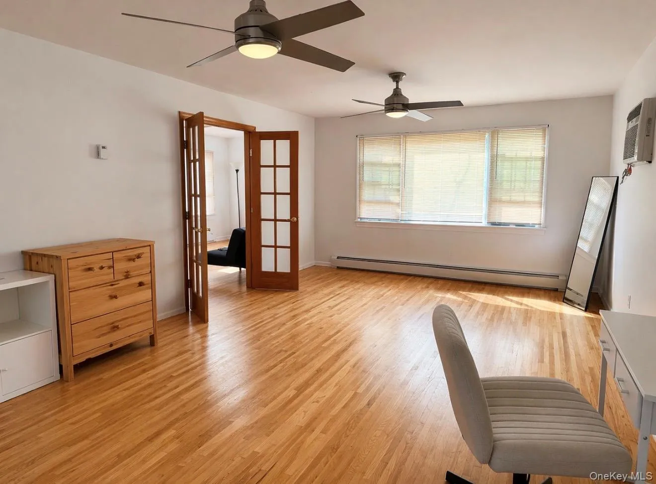 Spacious room featuring hardwood floors, two ceiling fans, and windows with blinds providing natural light Spacious room featuring hardwood floors, two ceiling fans, and windows with blinds providing natural light