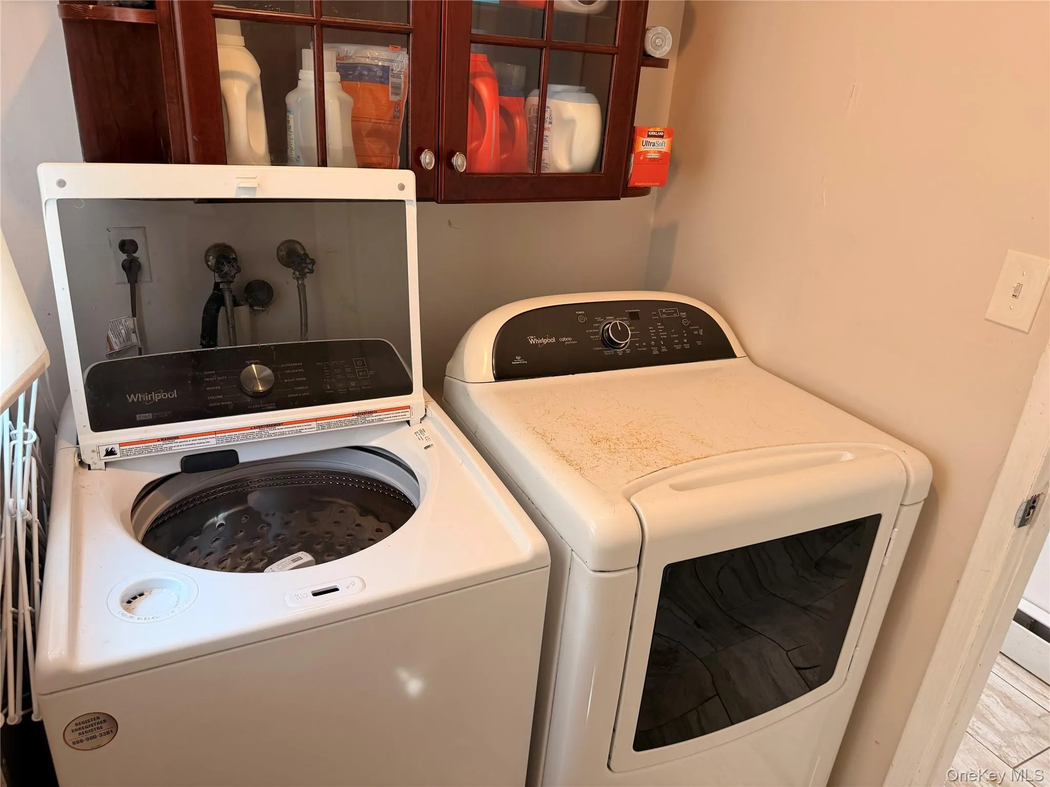 Laundry area featuring a top-loading washing machine, a dryer, and a wall-mounted wooden cabinet with glass-paneled doors Laundry area featuring a top-loading washing machine, a dryer, and a wall-mounted wooden cabinet with glass-paneled doors