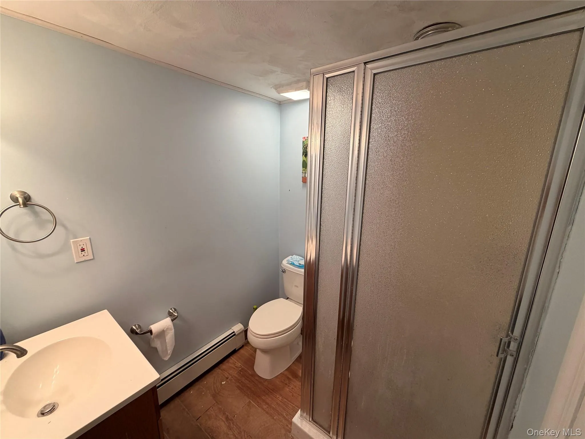 Bathroom featuring a vanity with a white countertop and a built-in sink, a toilet, and a glass-enclosed shower Bathroom featuring a vanity with a white countertop and a built-in sink, a toilet, and a glass-enclosed shower