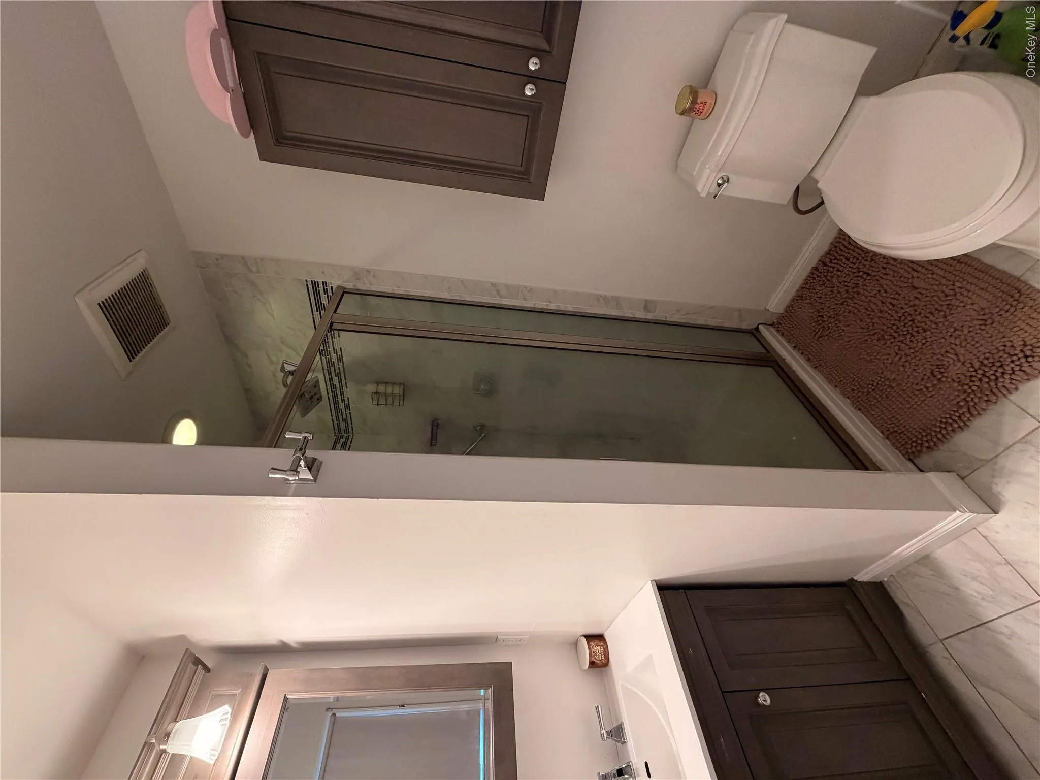 The bathroom features a vanity with an integrated sink, a glass-enclosed shower, a toilet, and wall-mounted cabinetry The bathroom features a vanity with an integrated sink, a glass-enclosed shower, a toilet, and wall-mounted cabinetry