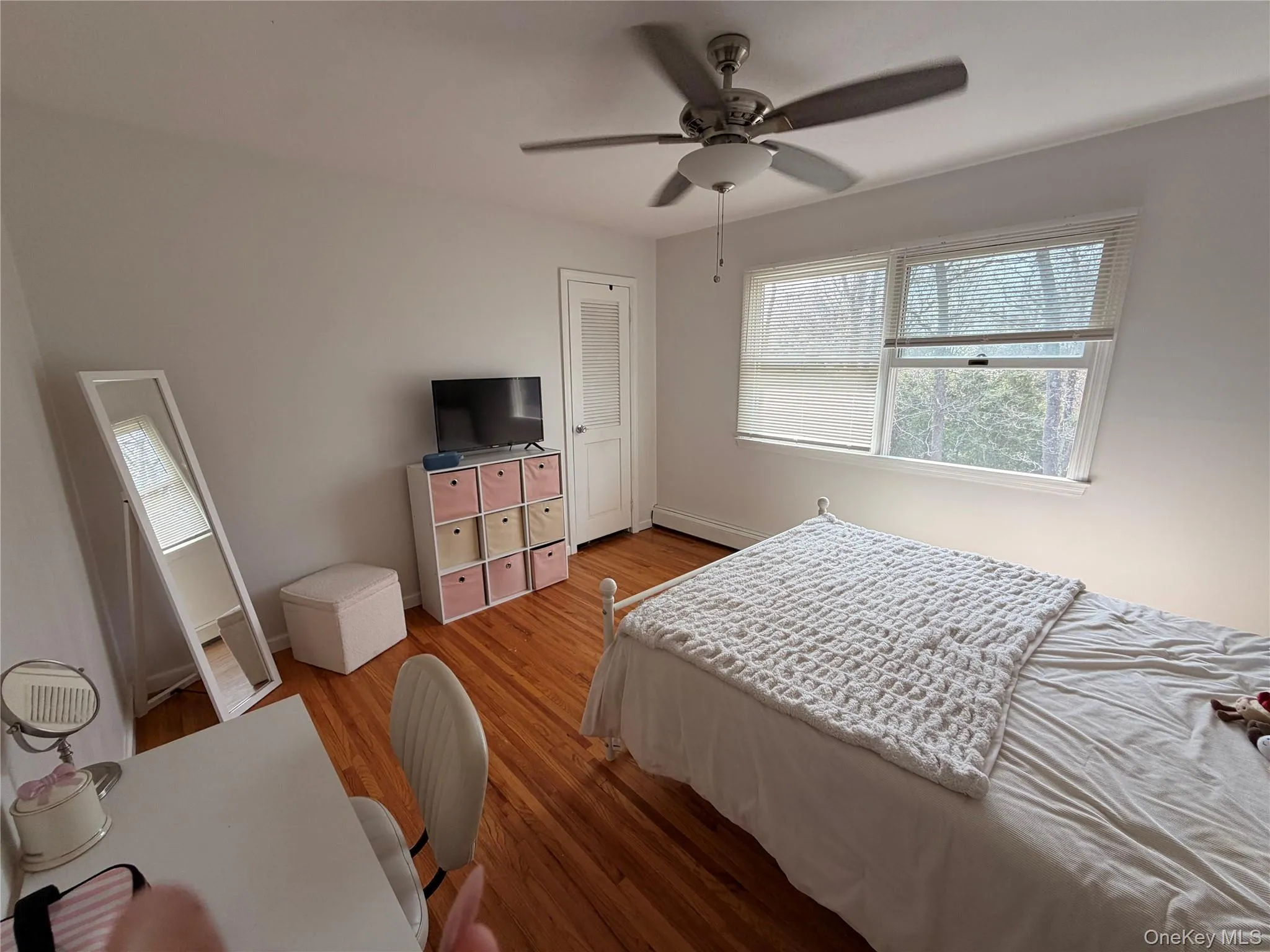 This room features hardwood flooring, a ceiling fan with integrated lighting, and two windows providing natural light This room features hardwood flooring, a ceiling fan with integrated lighting, and two windows providing natural light