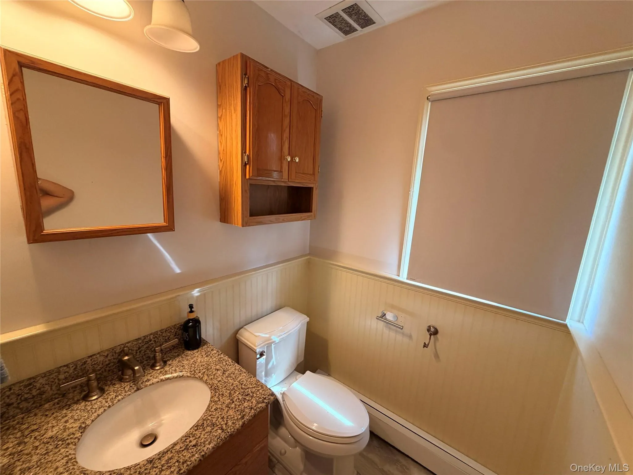 This bathroom features a vanity with a granite countertop and an oval sink, a wall-mounted wooden mirror, and a wood cabinet with upper storage and an open shelf This bathroom features a vanity with a granite countertop and an oval sink, a wall-mounted wooden mirror, and a wood cabinet with upper storage and an open shelf