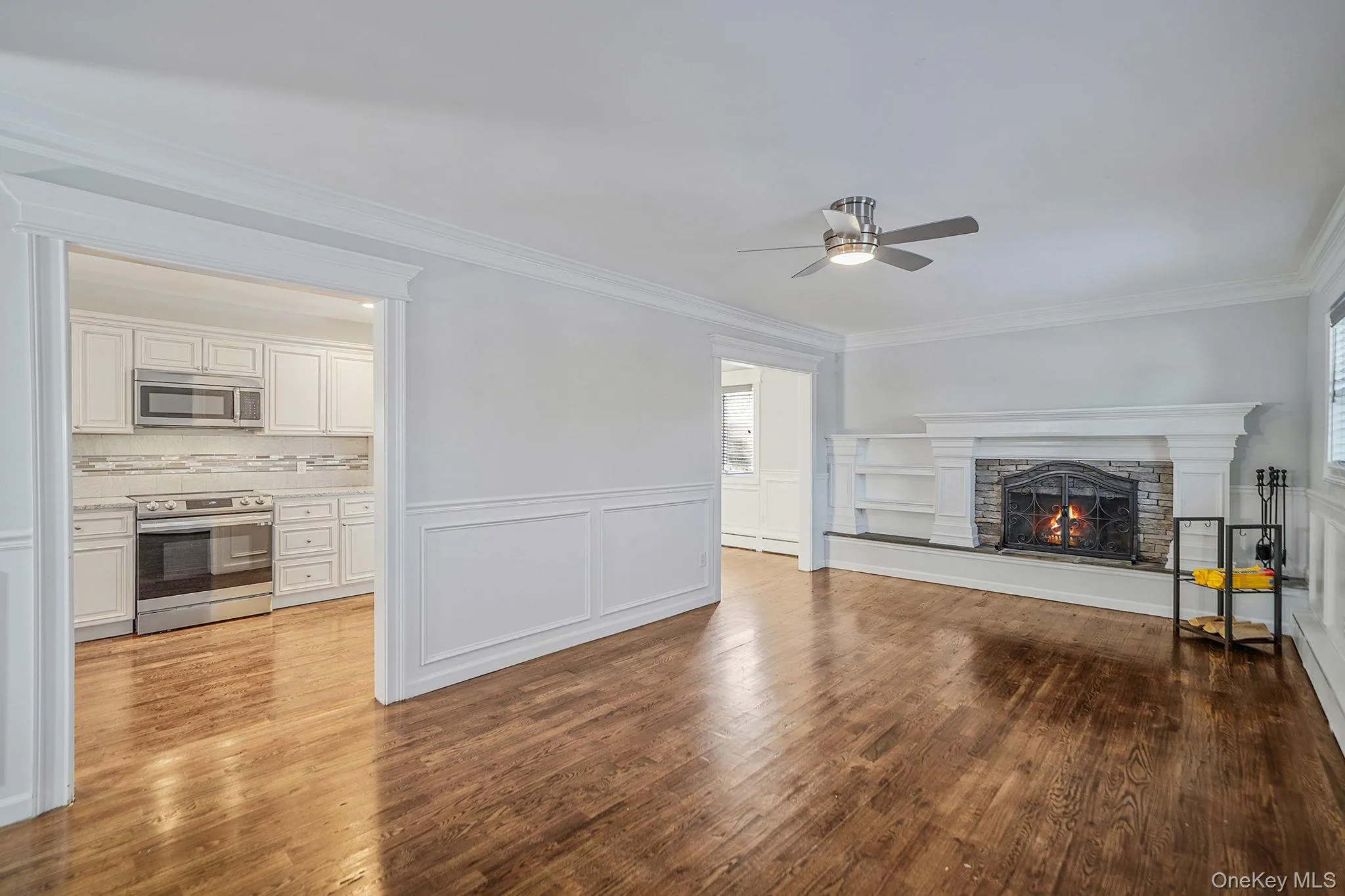 Living area featuring hardwood floors, a stone fireplace with a decorative mantel and built-in shelving, and a ceiling fan Living area featuring hardwood floors, a stone fireplace with a decorative mantel and built-in shelving, and a ceiling fan