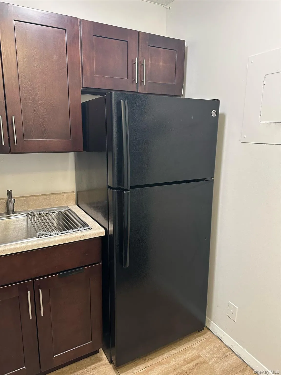Kitchen featuring baseboards, freestanding refrigerator, light countertops, and dark brown cabinets Kitchen featuring baseboards, freestanding refrigerator, light countertops, and dark brown cabinets