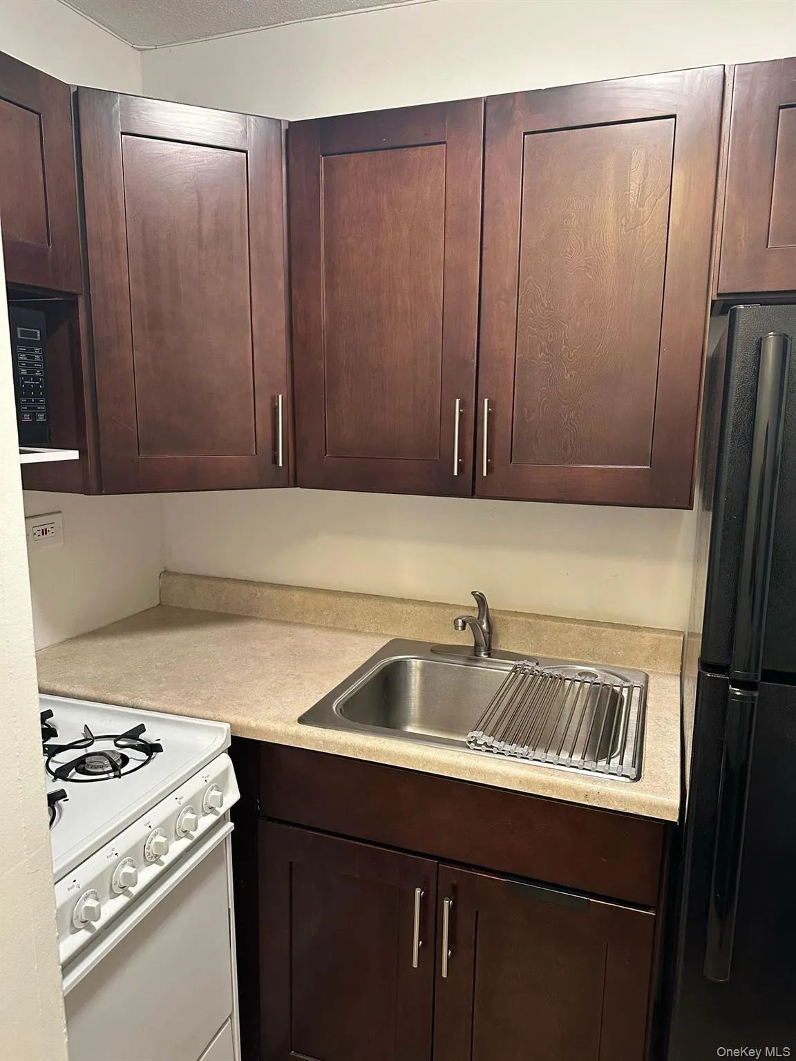 Kitchen featuring dark brown cabinetry, light countertops, freestanding refrigerator, white range with gas stovetop, and a sink Kitchen featuring dark brown cabinetry, light countertops, freestanding refrigerator, white range with gas stovetop, and a sink