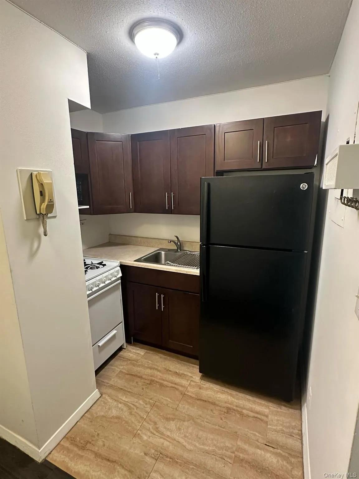 Kitchen with a sink, light countertops, freestanding refrigerator, dark brown cabinets, and white range with gas cooktop Kitchen with a sink, light countertops, freestanding refrigerator, dark brown cabinets, and white range with gas cooktop