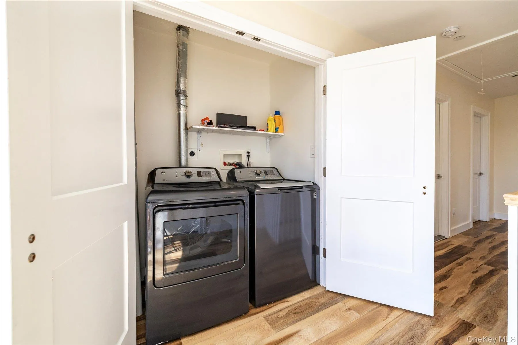 Dedicated laundry closet featuring a built-in shelf, appliance hookups, and wood-finish flooring Dedicated laundry closet featuring a built-in shelf, appliance hookups, and wood-finish flooring