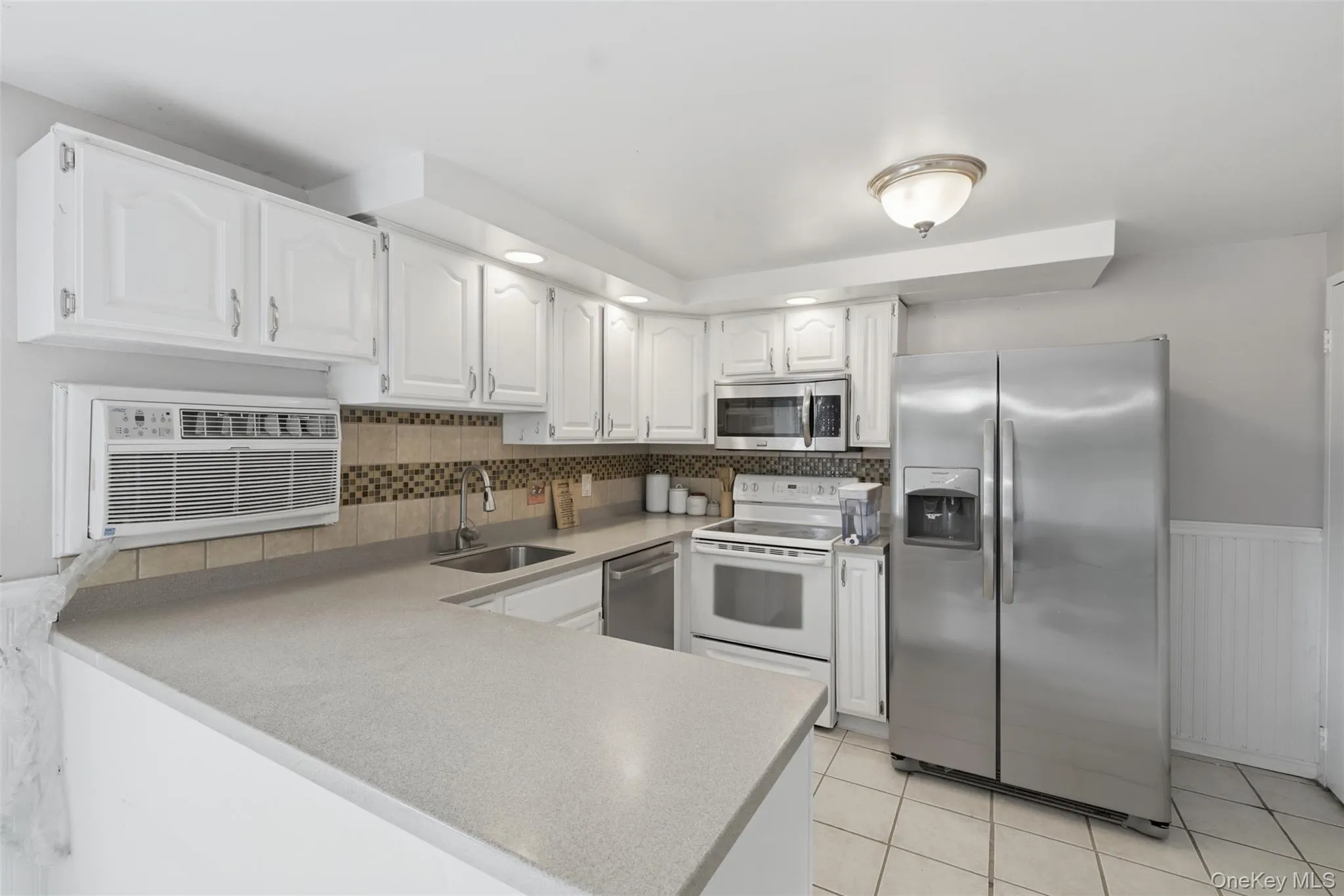 Kitchen featuring white cabinetry, light-toned countertops, and a mosaic tile backsplash Kitchen featuring white cabinetry, light-toned countertops, and a mosaic tile backsplash