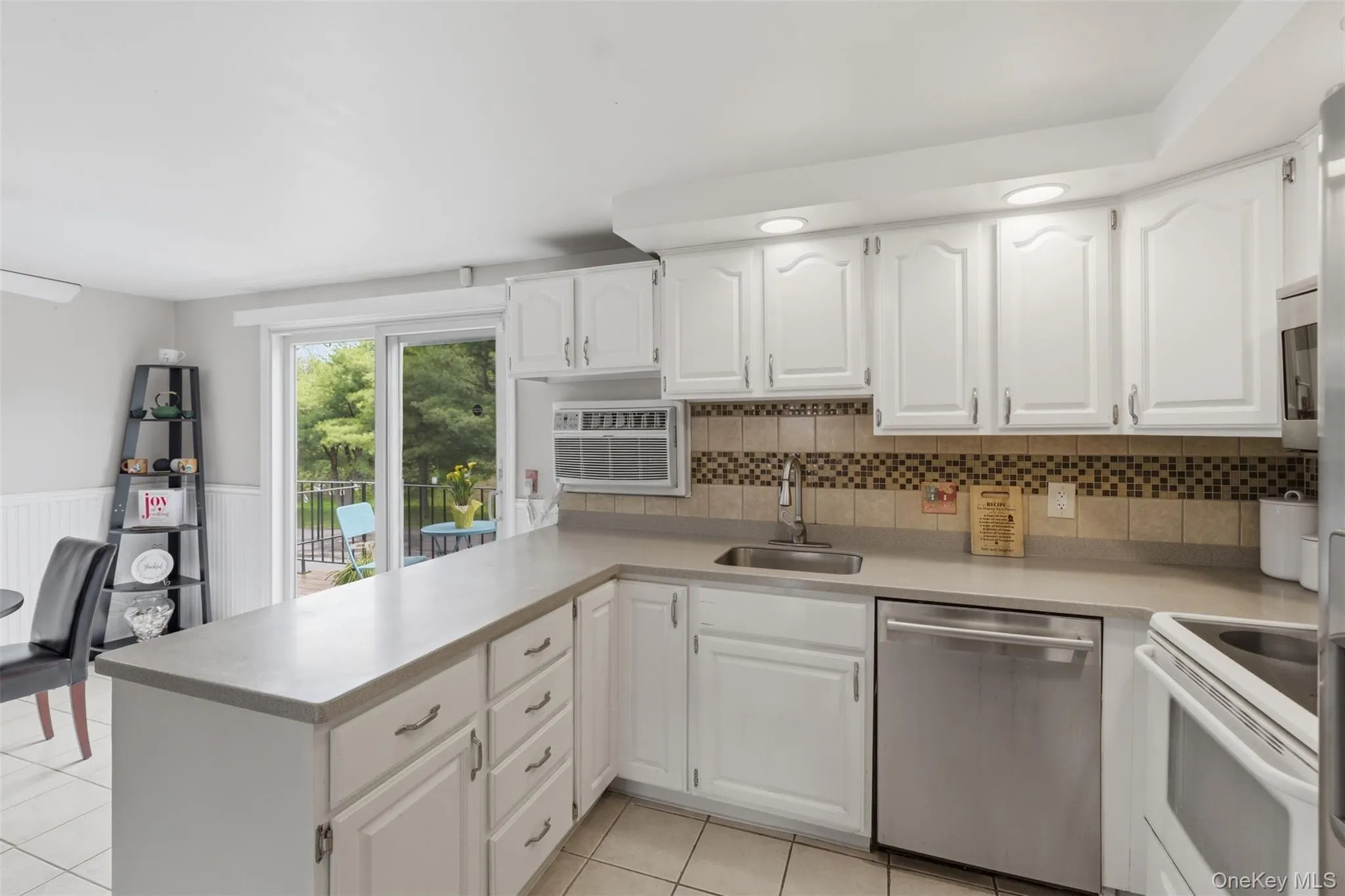 Kitchen featuring white cabinetry, light-toned countertops, a mosaic tile backsplash, stainless steel appliances, and tile flooring Kitchen featuring white cabinetry, light-toned countertops, a mosaic tile backsplash, stainless steel appliances, and tile flooring