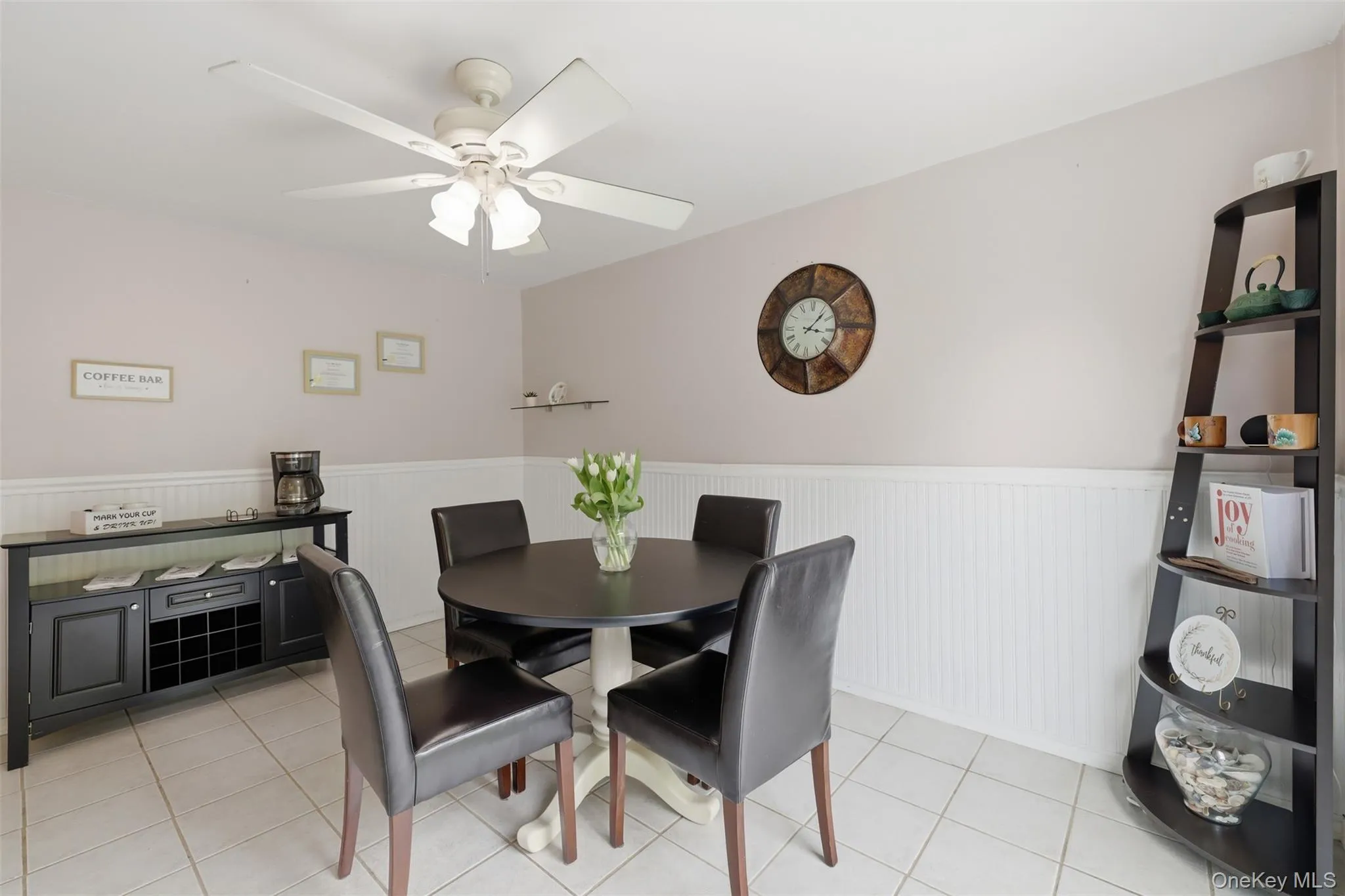 Dining area featuring tile flooring, wainscoting, a ceiling fan with integrated lighting, and neutral wall tones Dining area featuring tile flooring, wainscoting, a ceiling fan with integrated lighting, and neutral wall tones