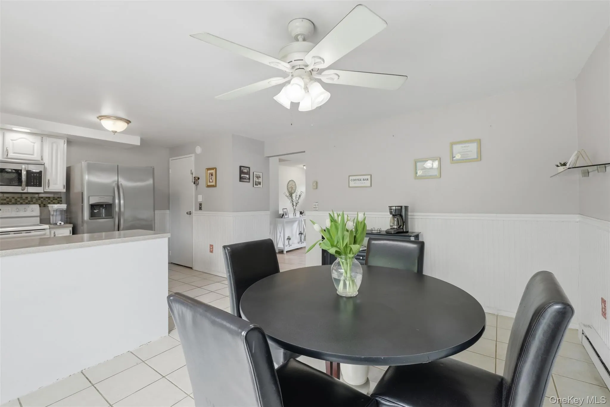Dining area featuring a ceiling fan with integrated lighting, tile flooring, and wainscoting Dining area featuring a ceiling fan with integrated lighting, tile flooring, and wainscoting