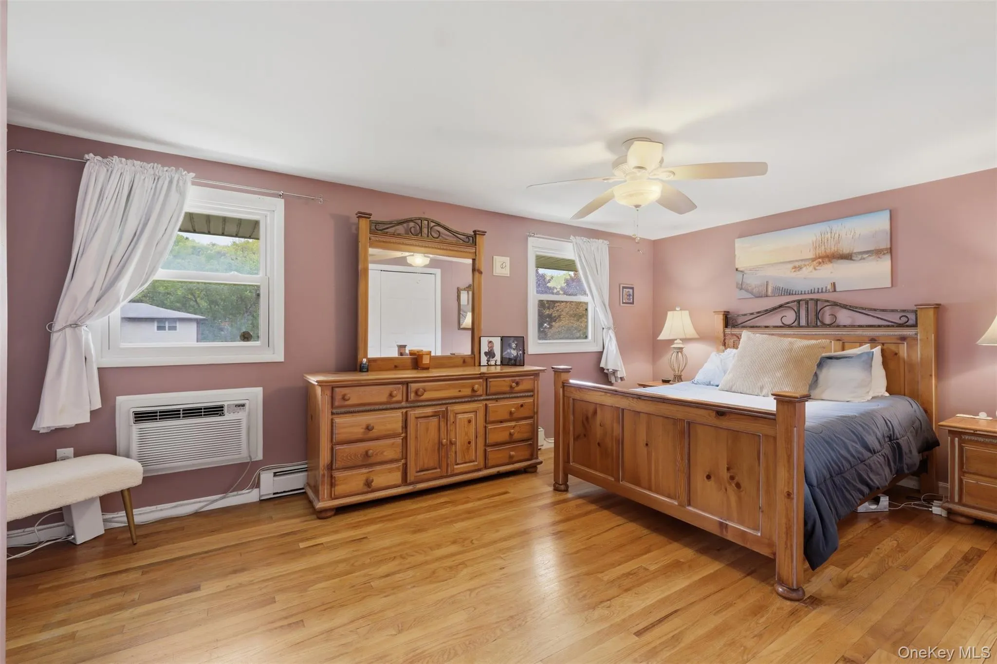 Hardwood flooring extends throughout this room, featuring multiple windows, a ceiling fan with integrated lighting, and baseboard heating Hardwood flooring extends throughout this room, featuring multiple windows, a ceiling fan with integrated lighting, and baseboard heating