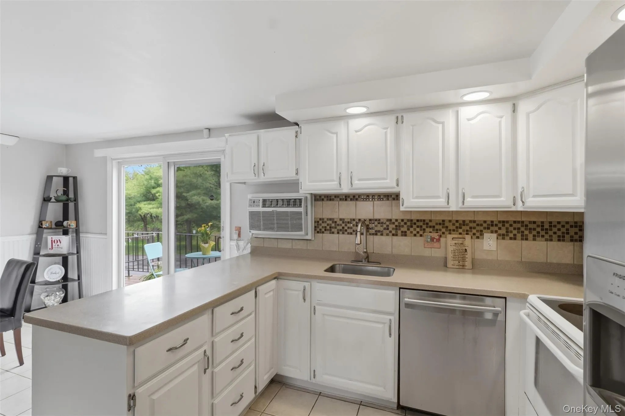 Kitchen featuring white cabinetry, light-toned countertops, a mosaic tile backsplash, and stainless steel appliances Kitchen featuring white cabinetry, light-toned countertops, a mosaic tile backsplash, and stainless steel appliances