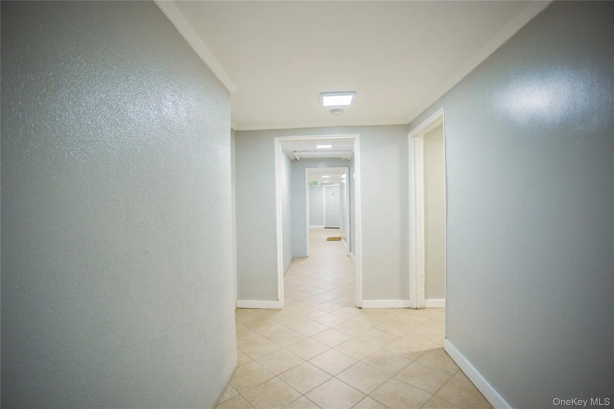 Hallway featuring baseboards, light tile patterned flooring, and crown molding Hallway featuring baseboards, light tile patterned flooring, and crown molding