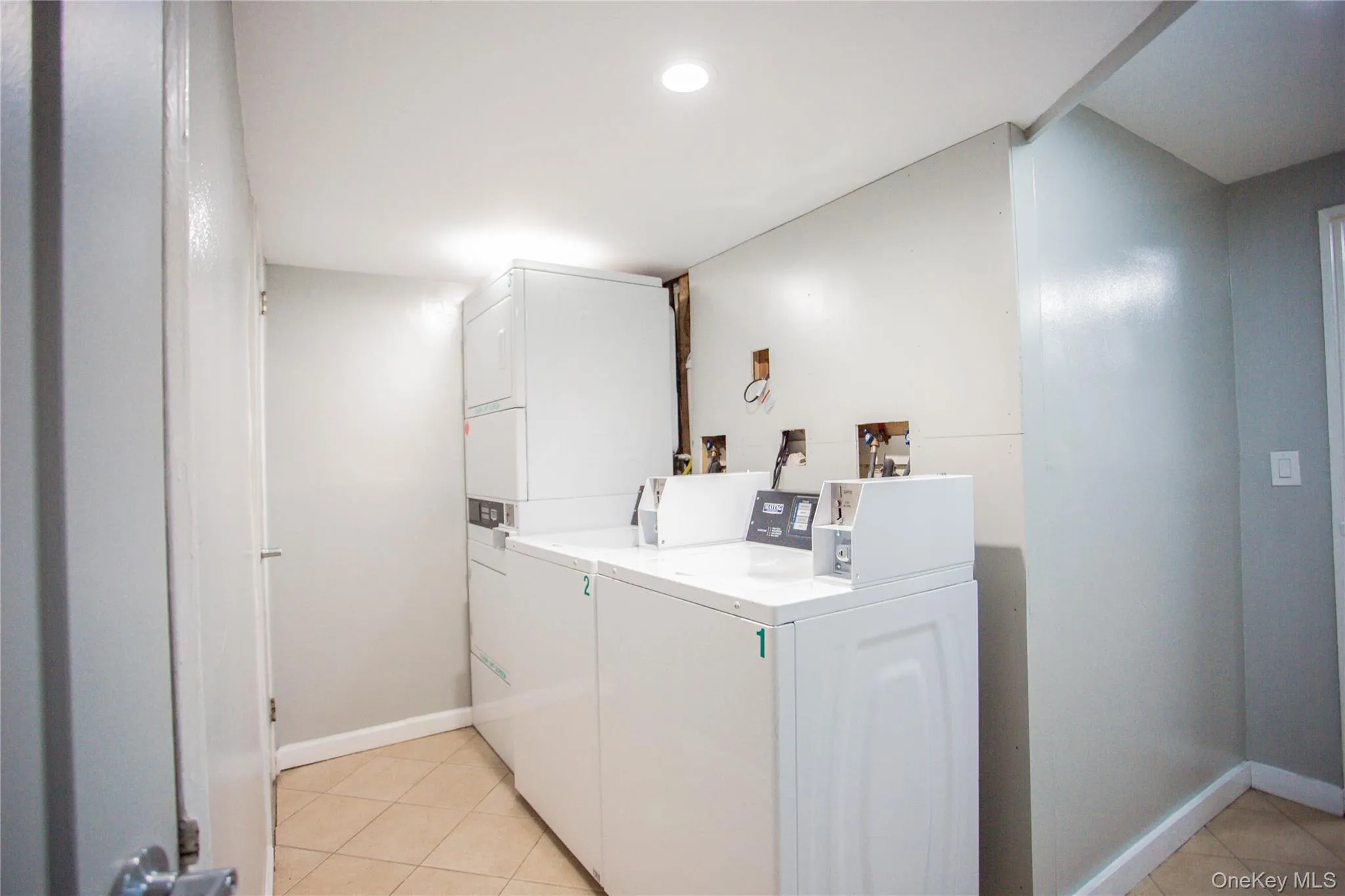 Community laundry room featuring washing machine and clothes dryer, baseboards, recessed lighting, stacked washing maching and dryer, and light tile patterned floors Community laundry room featuring washing machine and clothes dryer, baseboards, recessed lighting, stacked washing maching and dryer, and light tile patterned floors