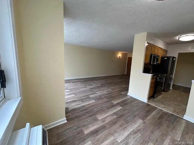 Kitchen featuring open floor plan, a textured ceiling, wood finished floors, and stainless steel appliances Kitchen featuring open floor plan, a textured ceiling, wood finished floors, and stainless steel appliances