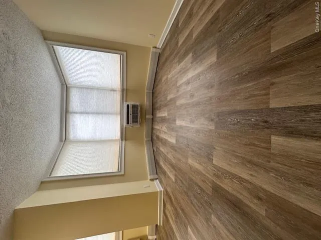 Empty room with an AC wall unit, baseboards, wood finished floors, and a textured ceiling Empty room with an AC wall unit, baseboards, wood finished floors, and a textured ceiling