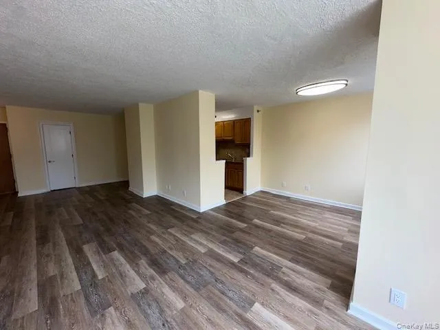 Unfurnished room featuring dark wood-style floors, a textured ceiling, and baseboards Unfurnished room featuring dark wood-style floors, a textured ceiling, and baseboards